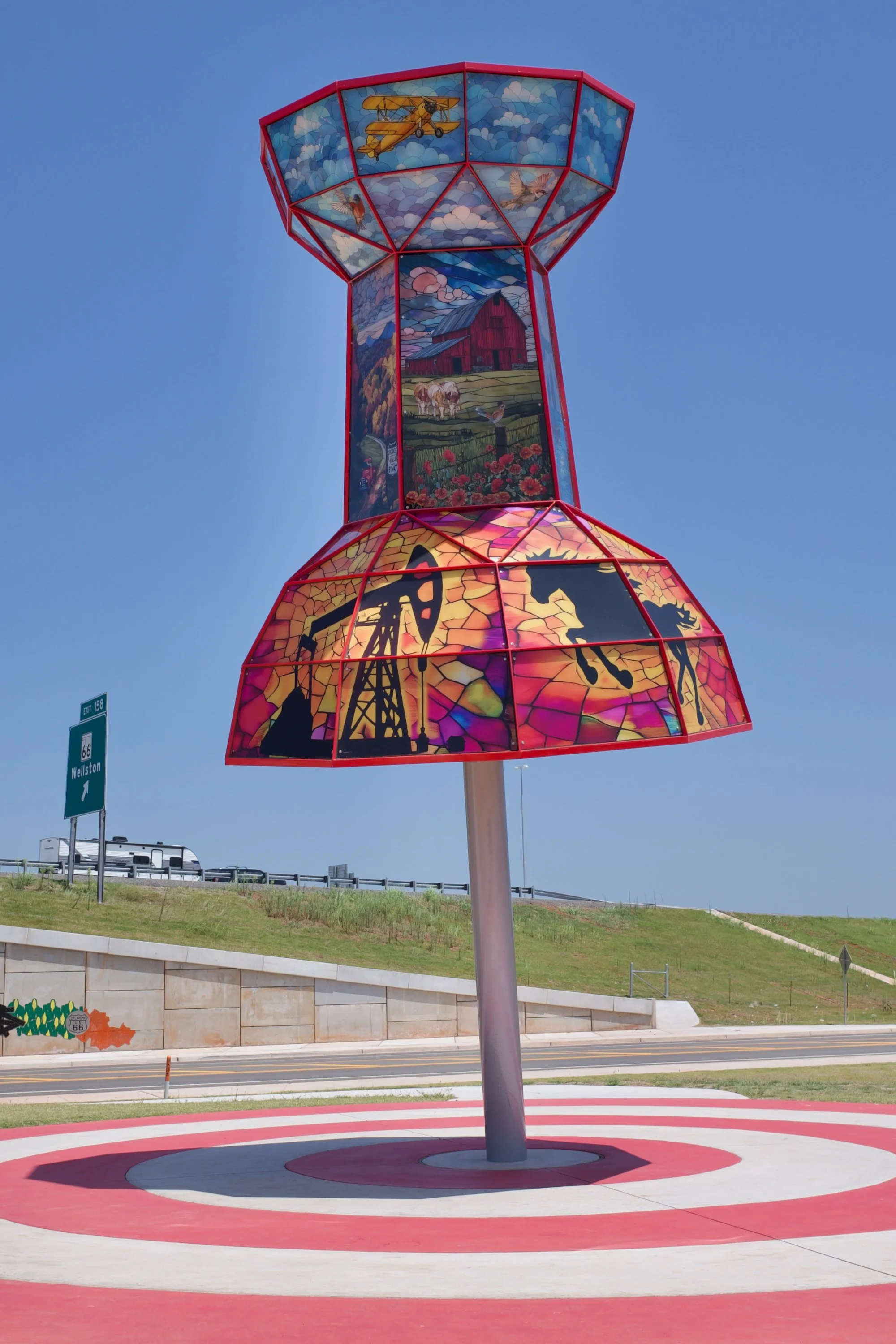 A giant, 23-foot-tall illuminated map push pin titled 'You Are Here' standing upright as a roadside art installation in Wellston, Oklahoma, marking the midpoint of Route 66 in the state.
