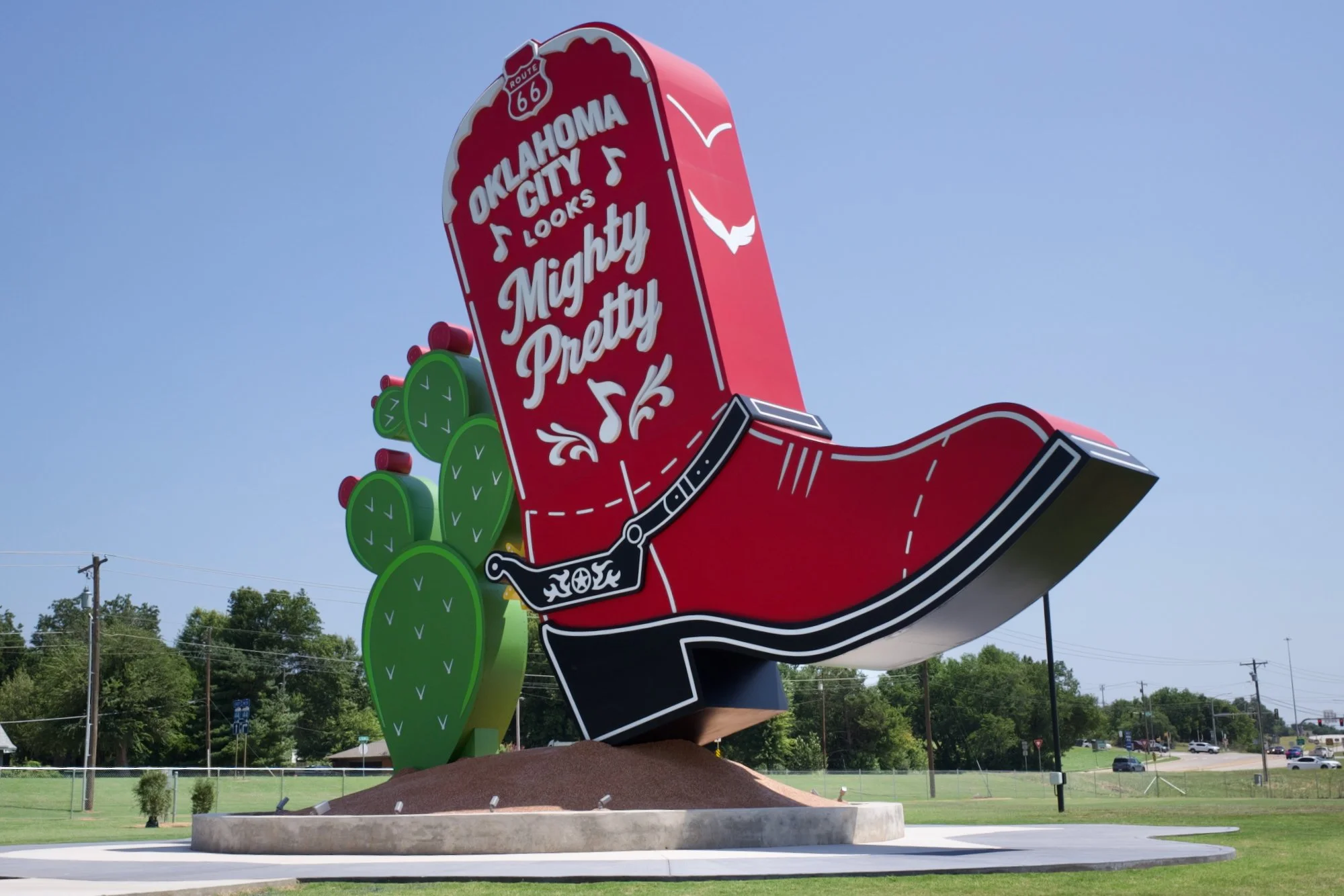 A towering 35-foot-tall red cowboy boot sculpture titled Kicks 66, featuring illuminated details and a companion prickly pear cactus, standing in the parking lot of the National Cowboy & Western Heritage Museum in Oklahoma City as a tribute to Route 