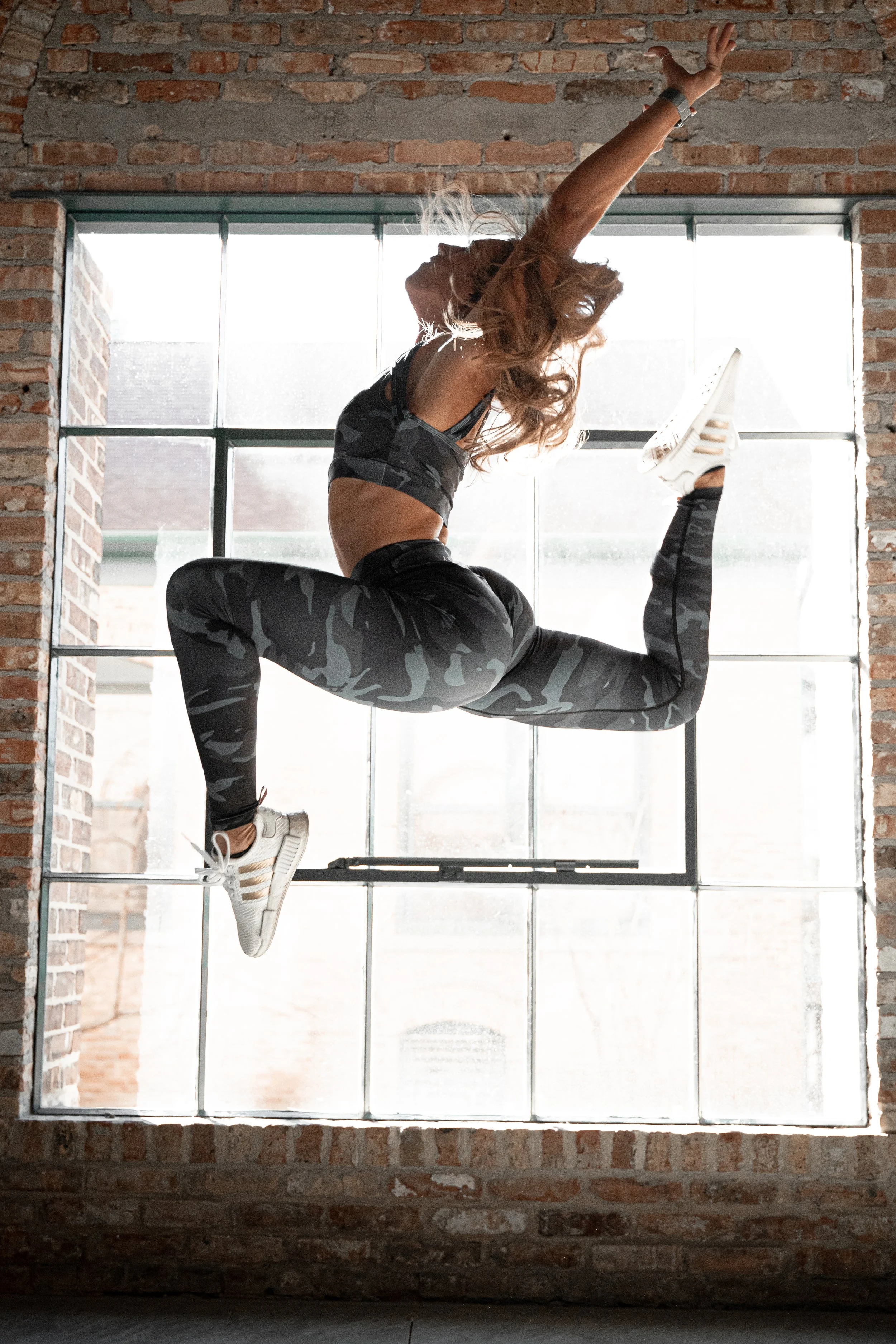 A woman in workout clothes performs a martial arts move on a large window with a brick wall background.