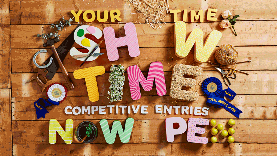 Colorful letters spelling out "Your Show Time" and "Competitive Entries Now" on a wooden background, with ribbons, scissors, and craft supplies around them.