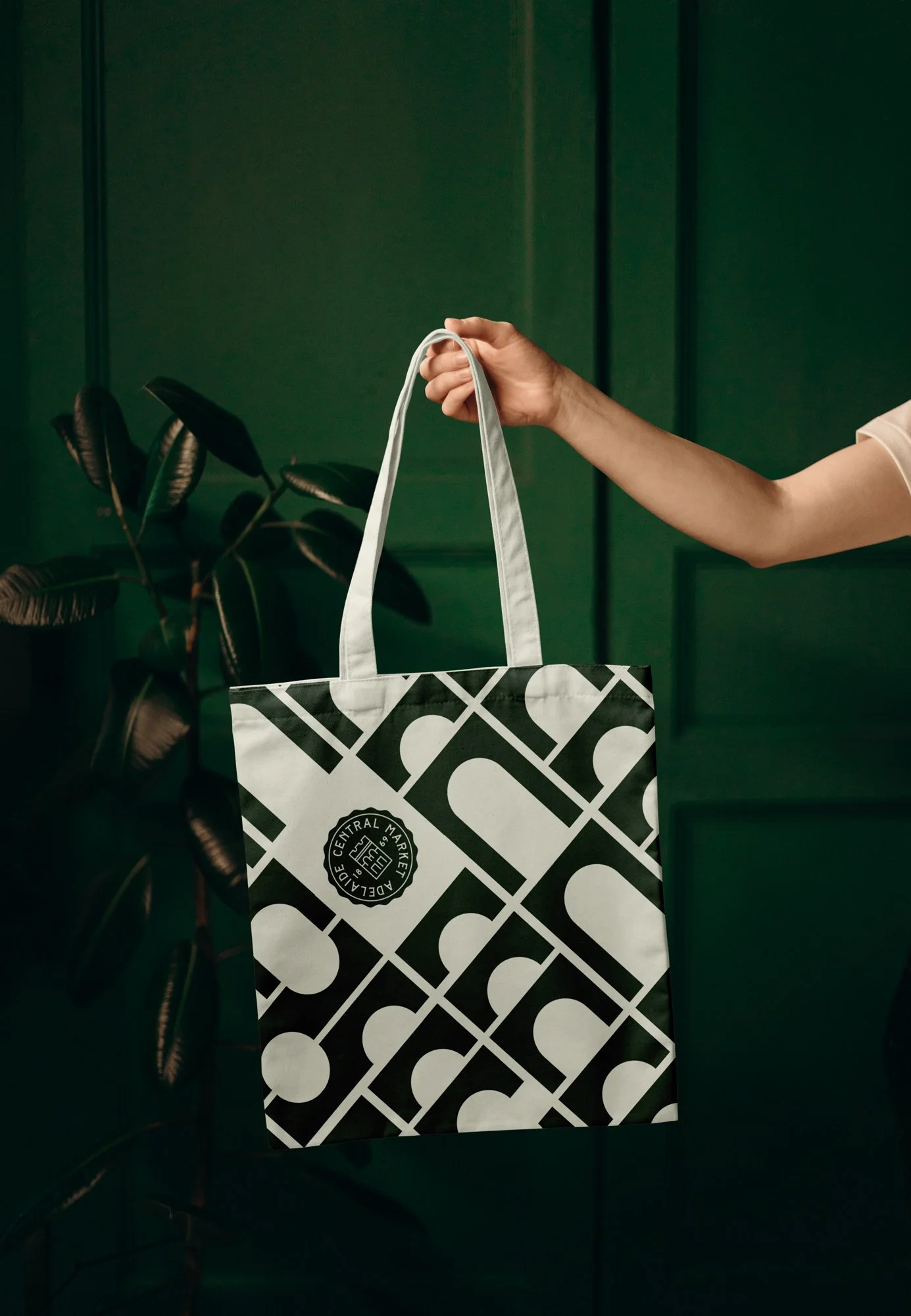 Person holding a black and white patterned tote bag with the logo "Central Market" against a green wall background.