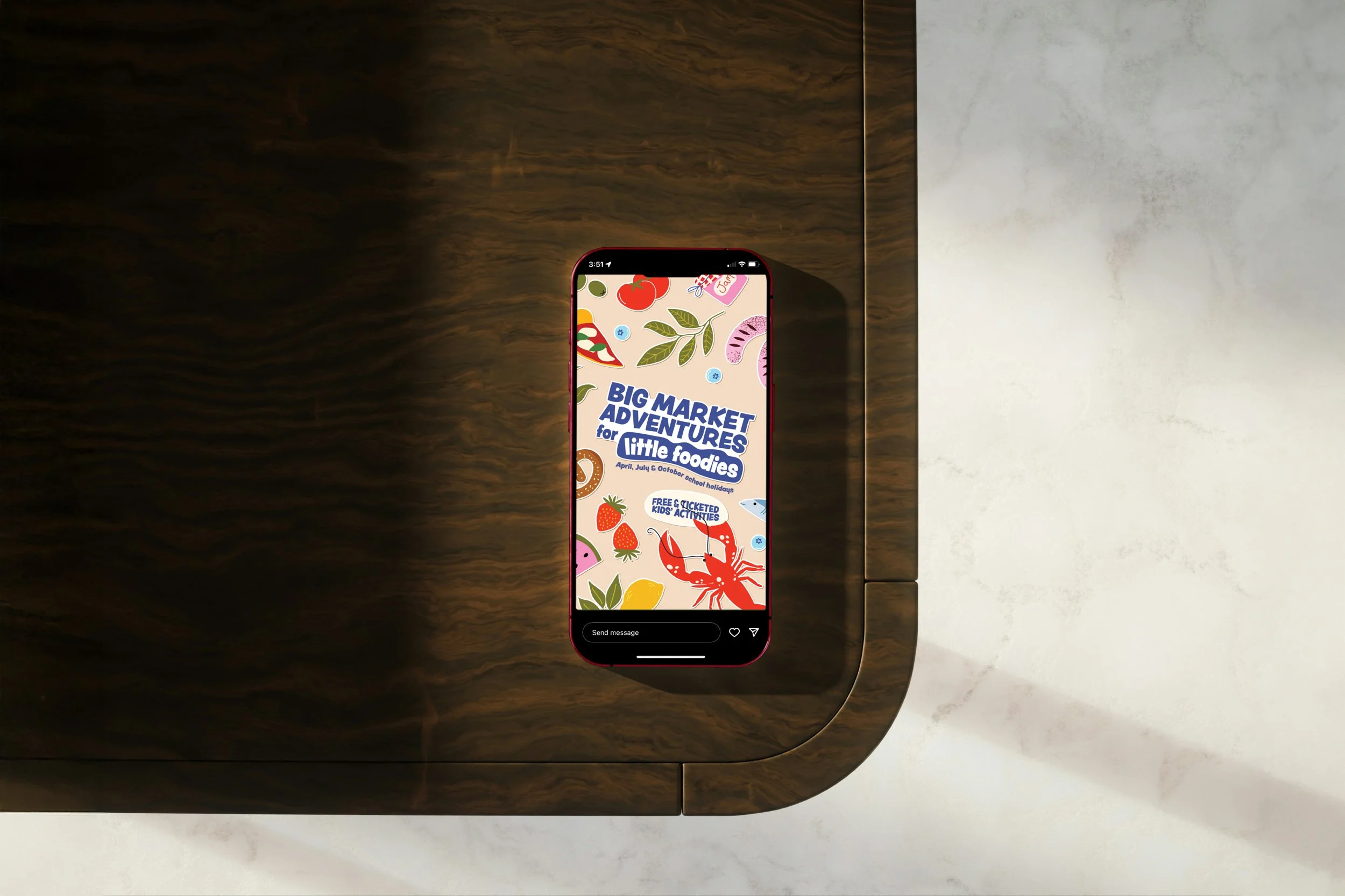 Smartphone on a wooden table showing a colorful promotional graphic for a market event with food illustrations and text about kids' activities.