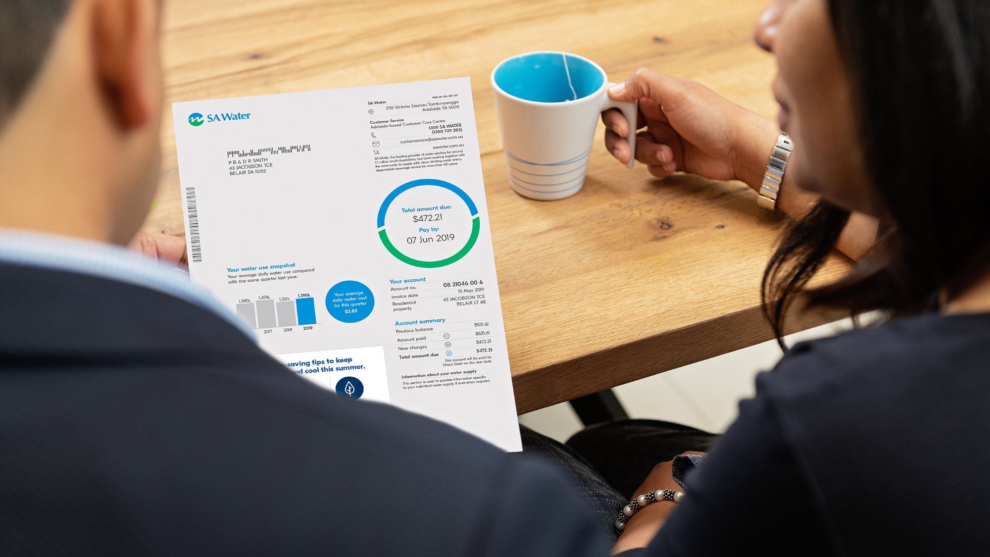 A man and woman reviewing a water bill together at a wooden table, with a coffee mug nearby.