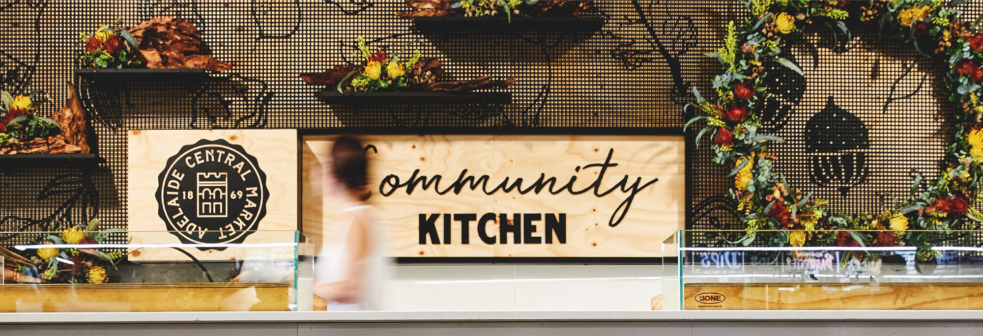 Sign for the community kitchen with floral arrangements and a blurred person in front.