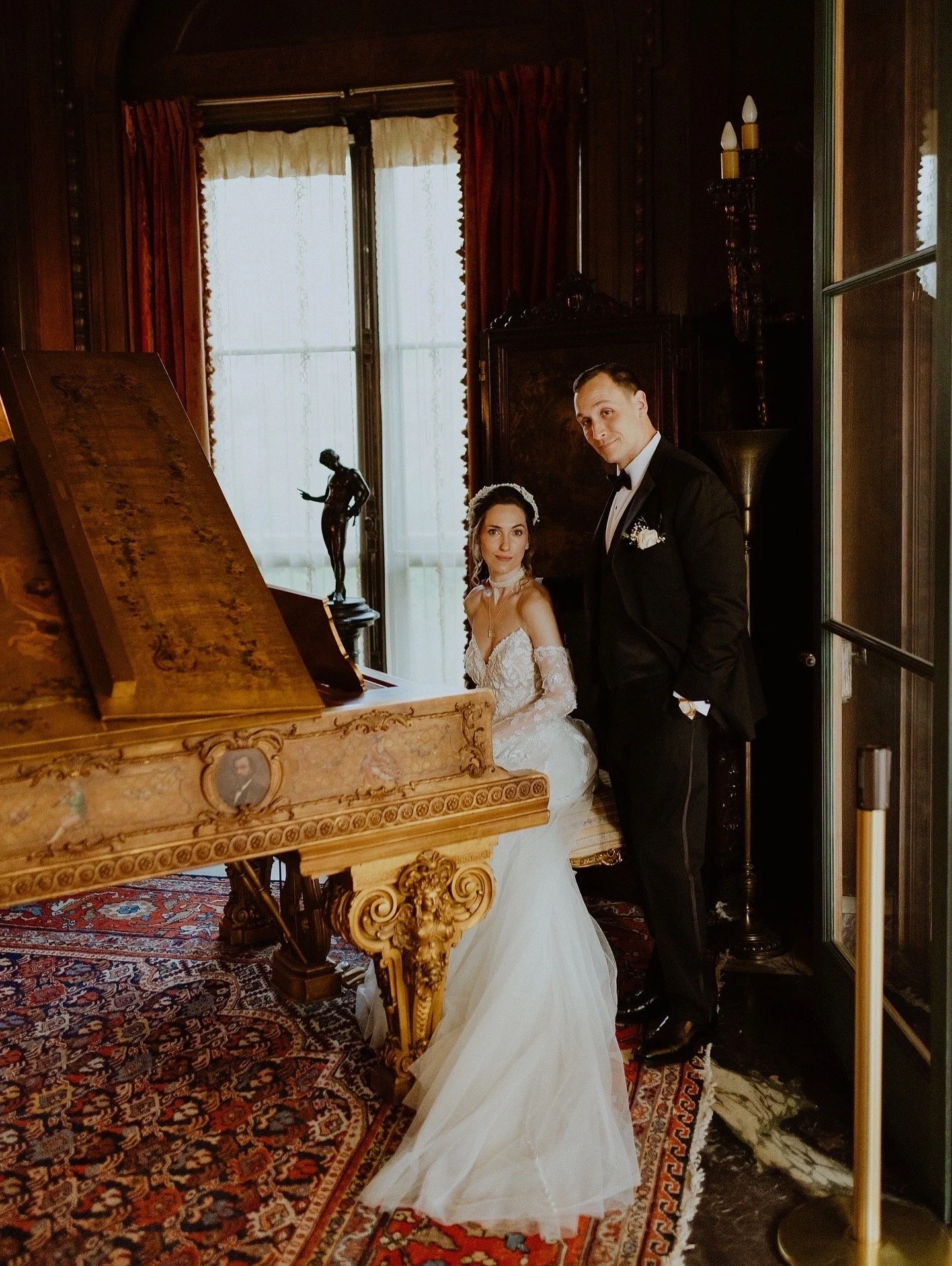 A bride and groom dressed in wedding attire in an elegant, vintage-style room with ornate furniture and a piano.