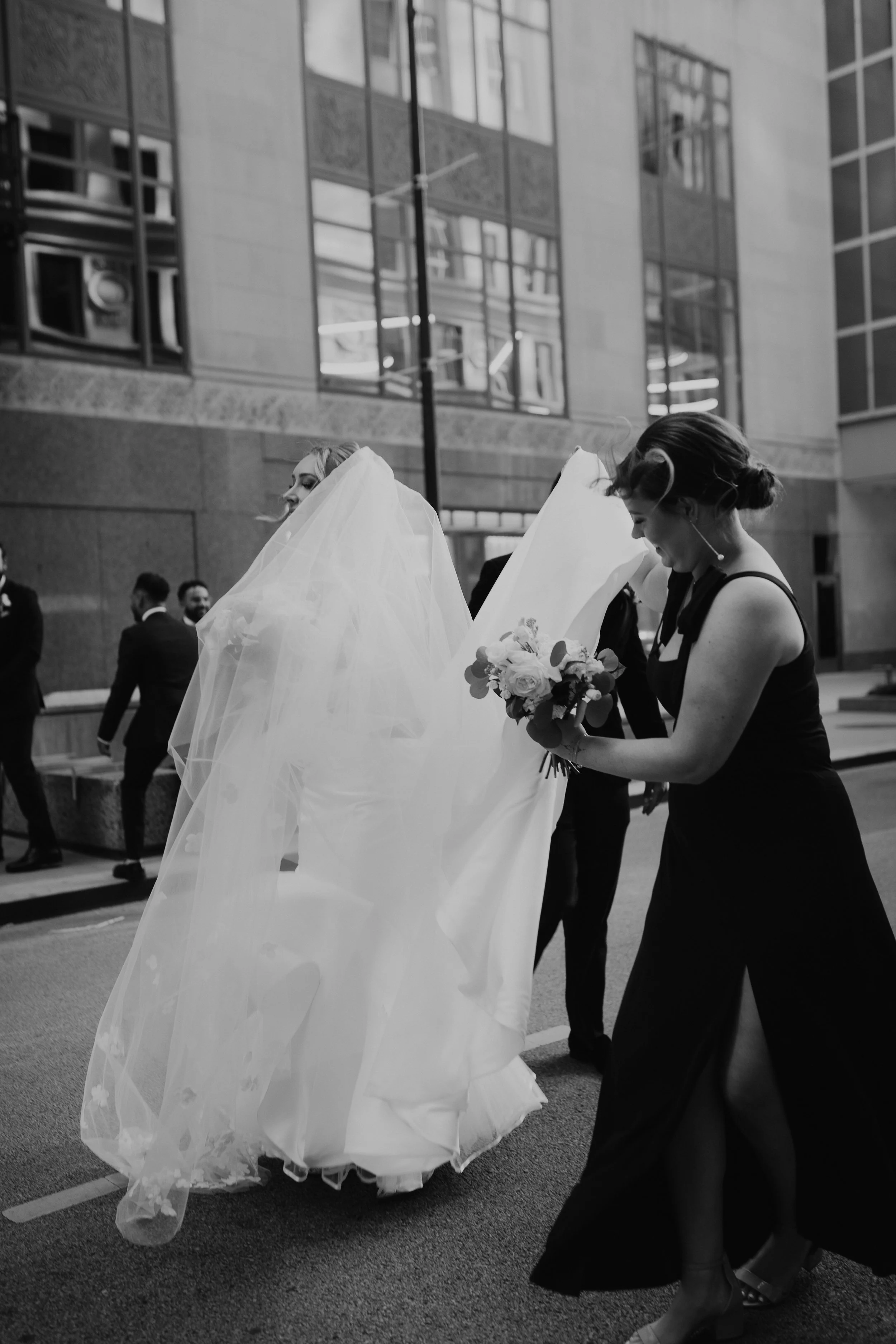 Chicago bride walking in the street with her bridesmaids carrying her bouquet and veil