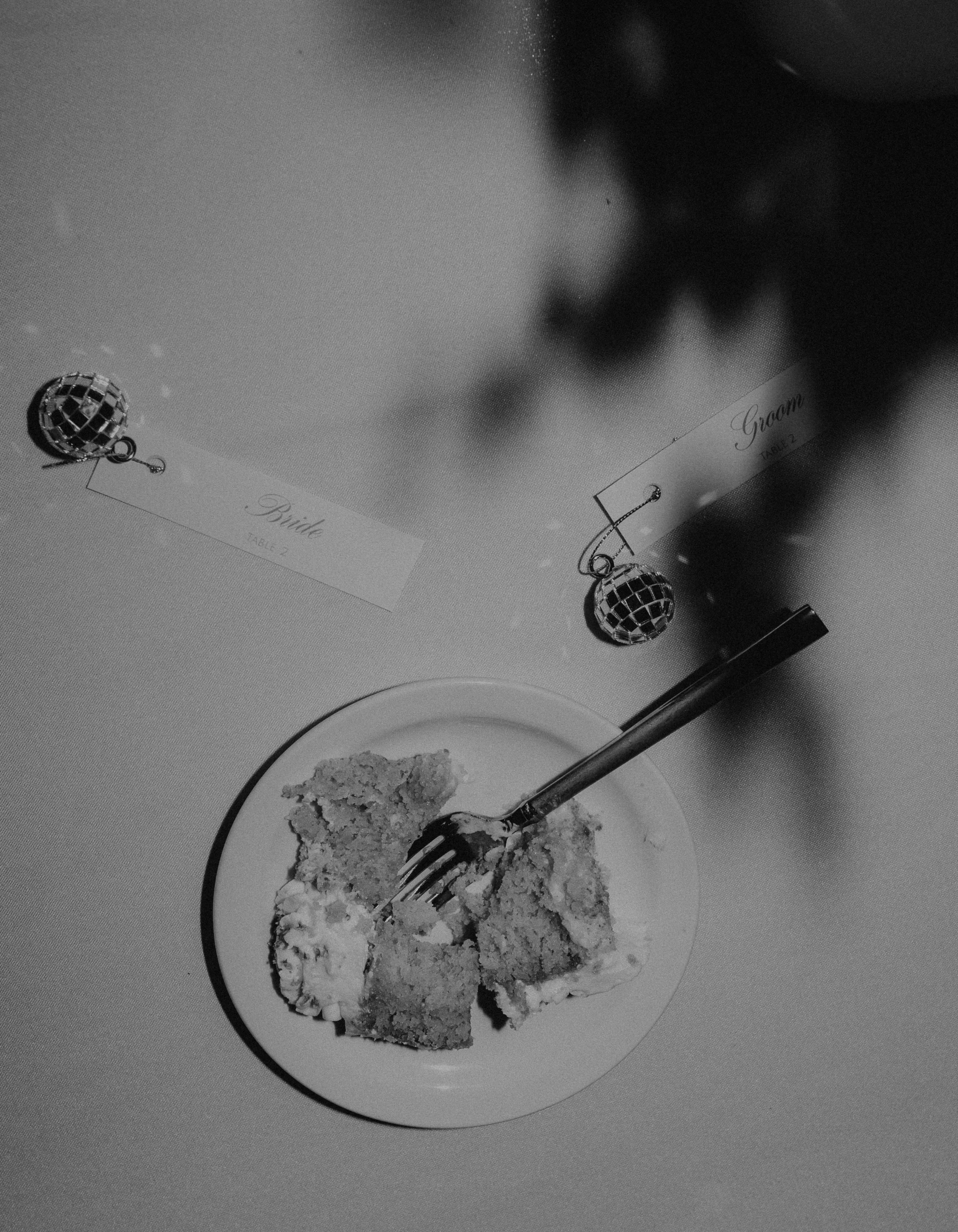A plate with pieces of cake and a fork on top of the cake. Two small chairs with labels reading 'Bride' and 'Groom' are placed on the table, at their wedding celebration at Bottom Lounge Chicago