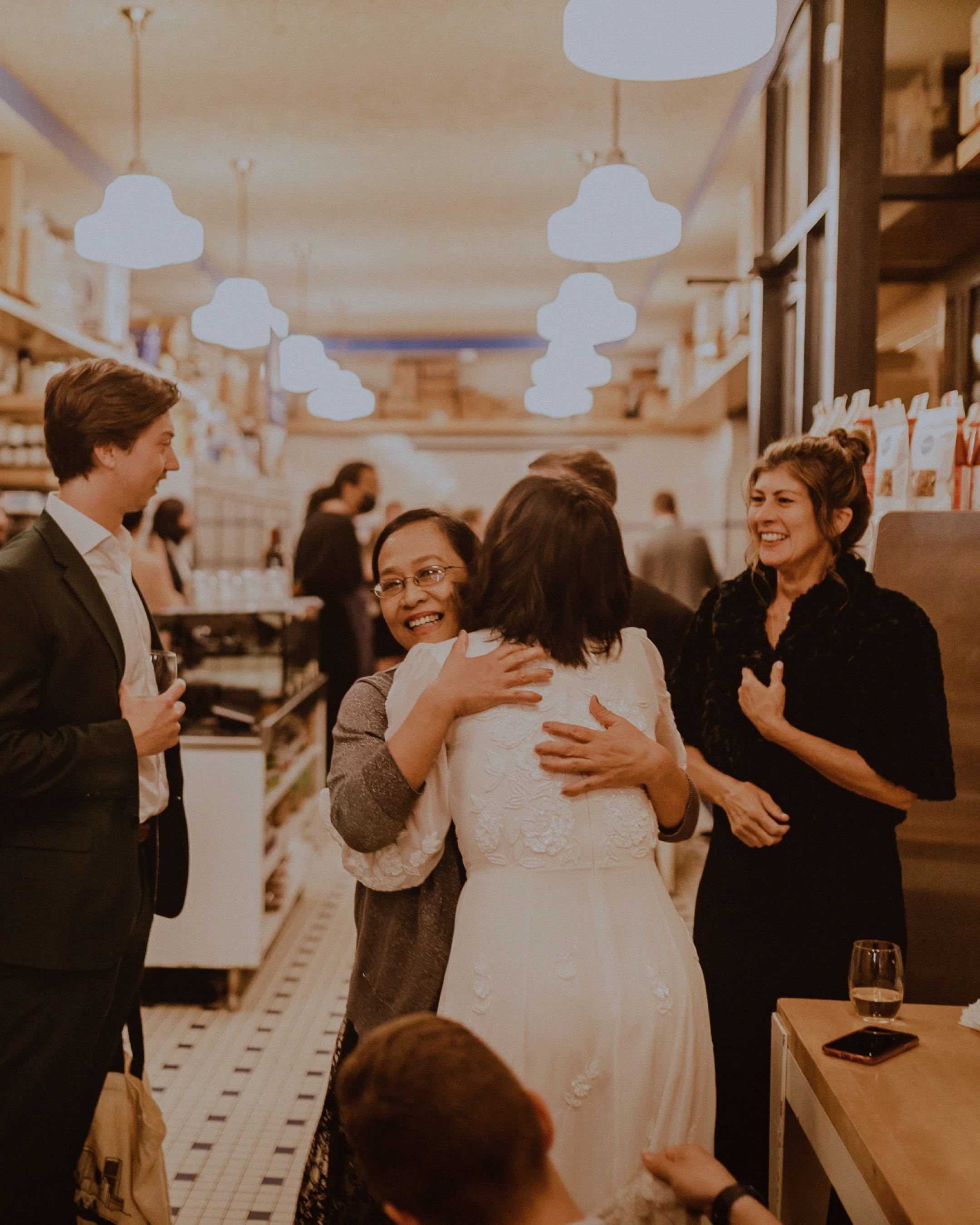 People hugging and smiling at a social gathering in a warmly lit restaurant Publican Quality Meats in Fulton Market Chicago. Elopement Photography by Ttolbphotog