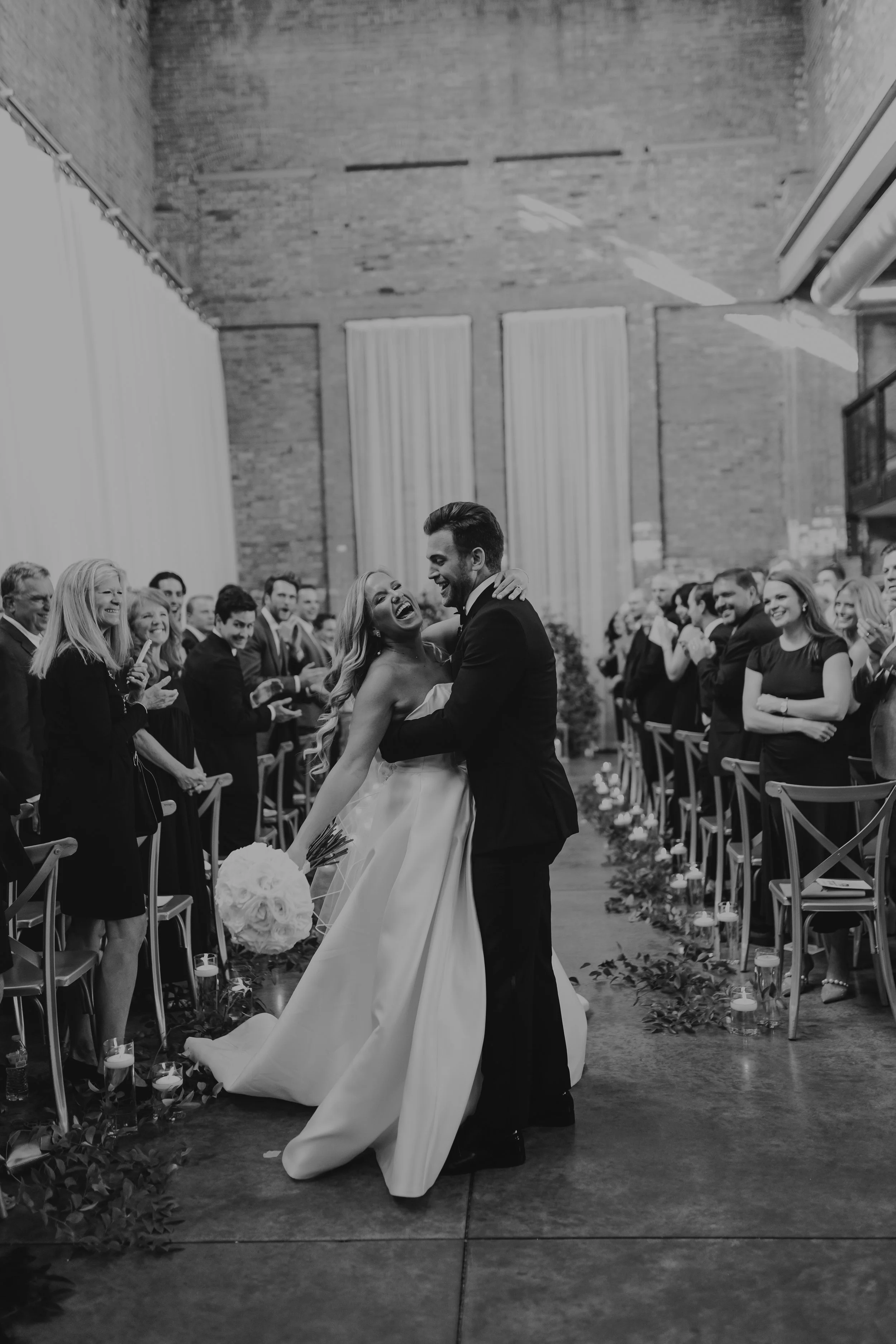 A joyful bride and groom dancing at their wedding reception, surrounded by guests in a spacious, industrial-style venue with exposed brick walls and tall windows at The Fairlie Wedding Venue in Chicago IL - Wedding Photography by Ttolbphotog.com
