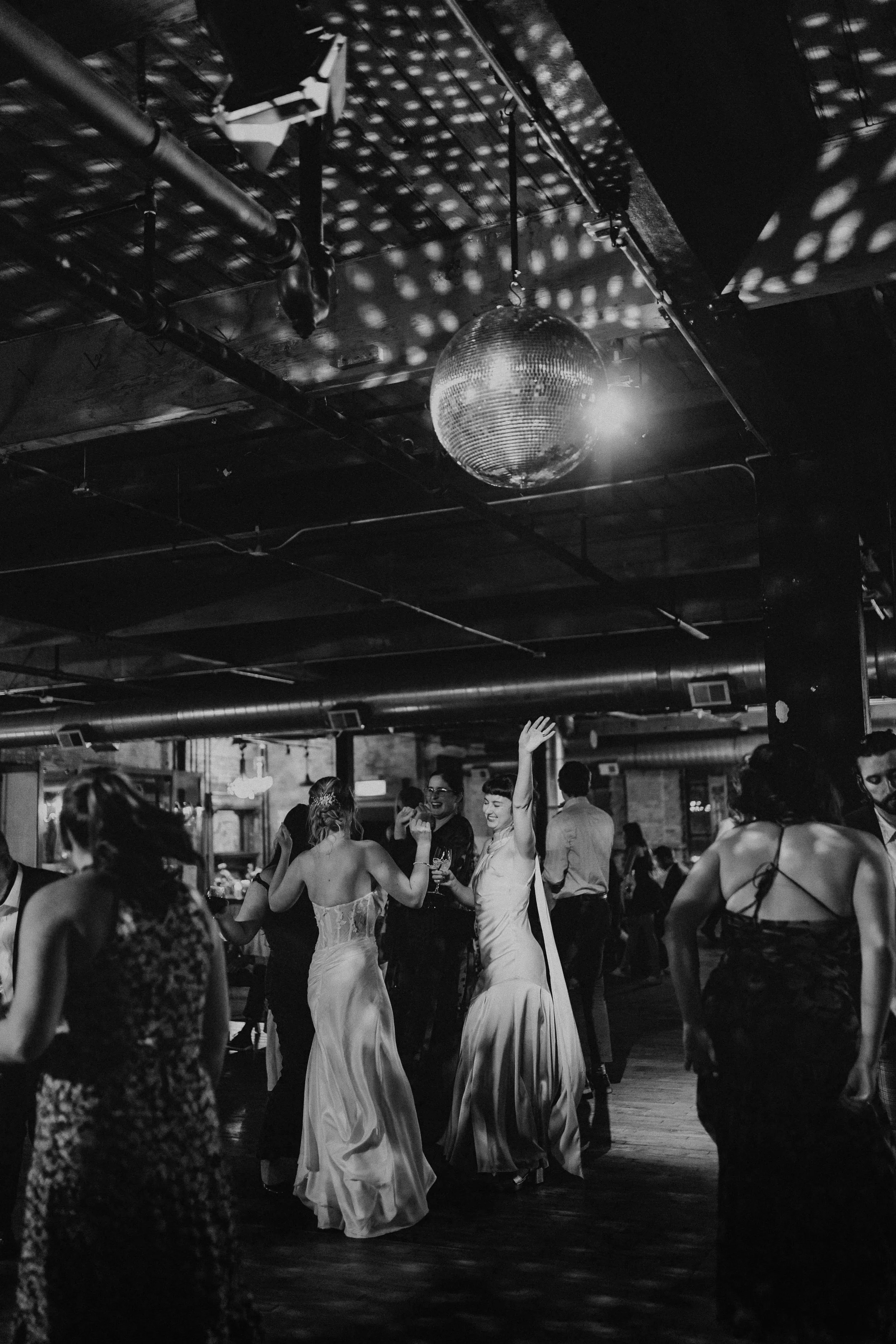 People dancing and socializing at an indoor wedding party with a disco ball hanging from the ceiling at Salvage One Events.