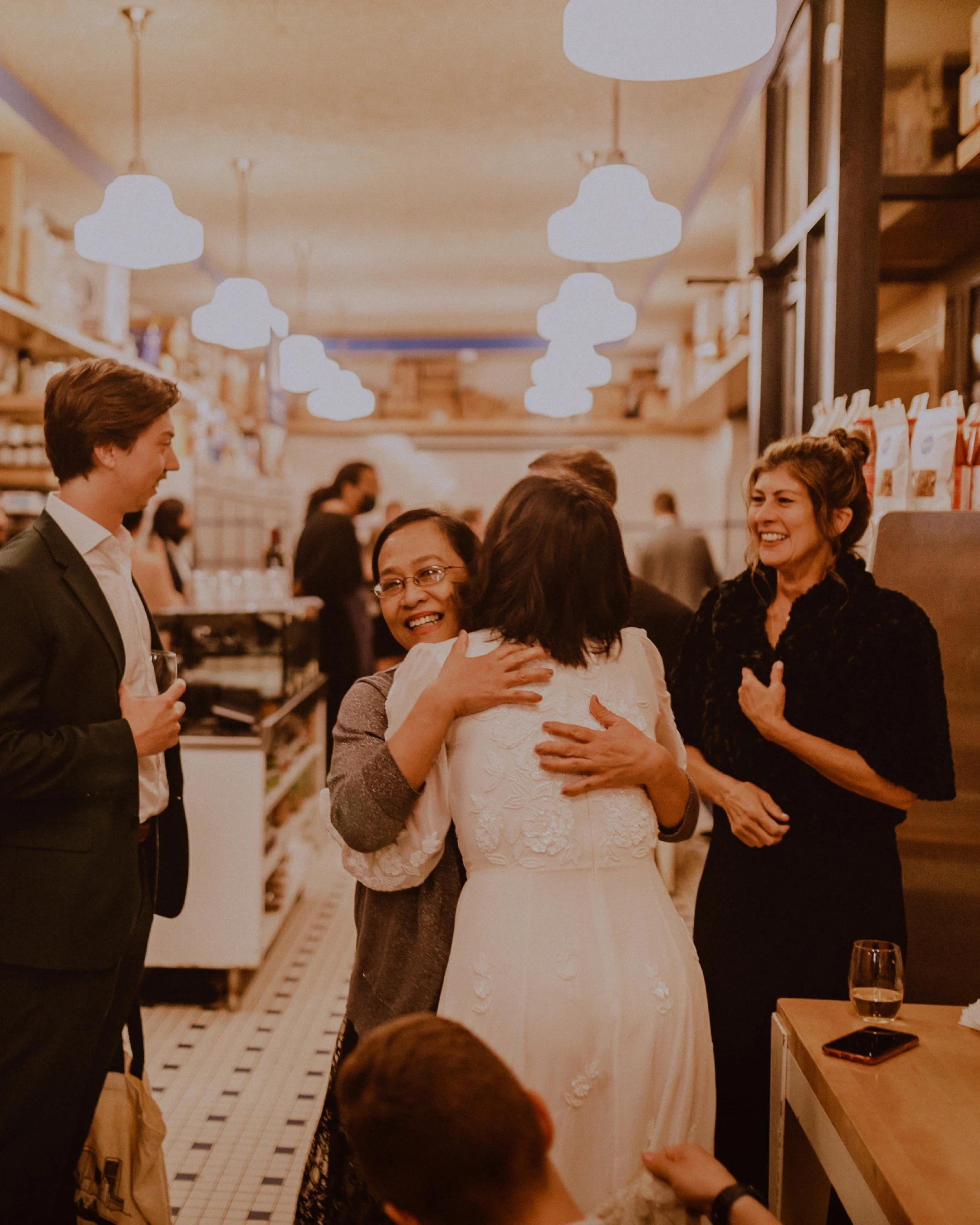People hugging and smiling at a social gathering in a warmly lit restaurant Publican Quality Meats in Fulton Market Chicago. Elopement Photography by Ttolbphotog