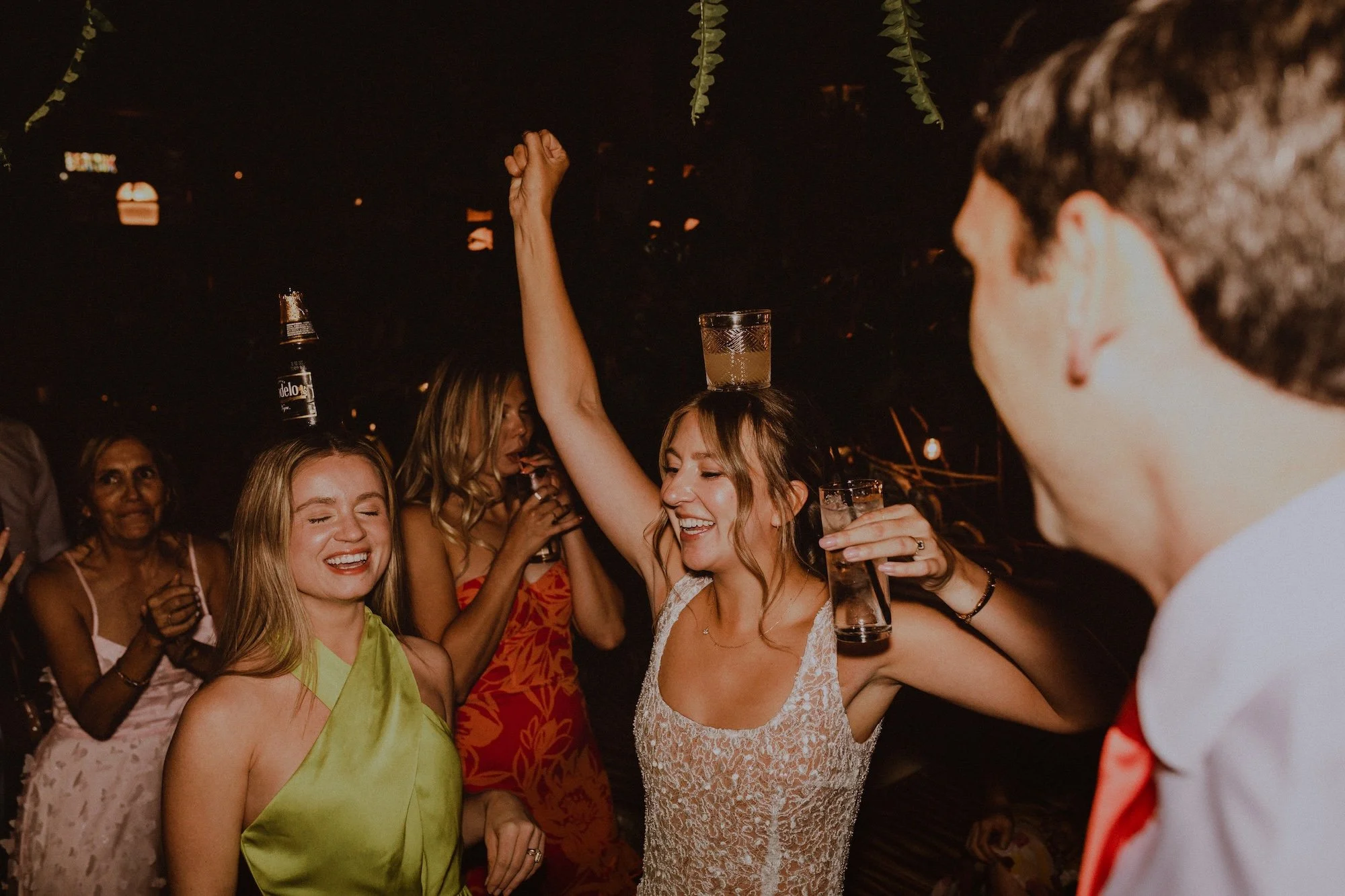 Group of people dancing and celebrating at wedding reception, with two woman balancing a glass on their head and surrounded by friends. Beatnik West Town Wedding Chicago IL