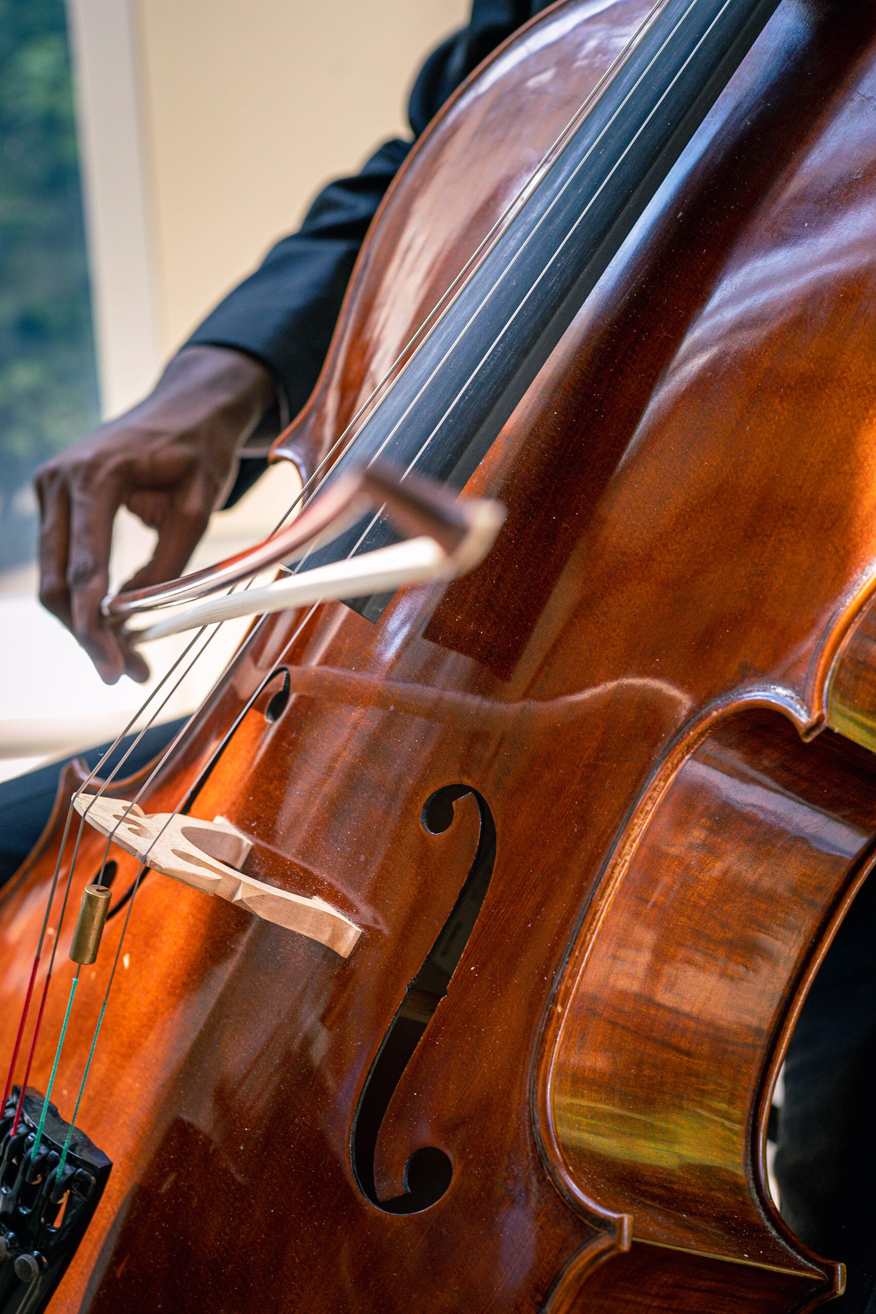 Close-up of a person playing a wooden cello, focusing on the instrument and the musician's hand holding a bow.
