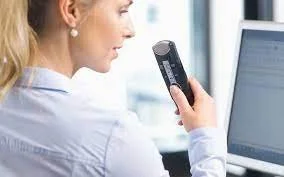 A woman speaking into a dictation device with a computer screen in front of her.
