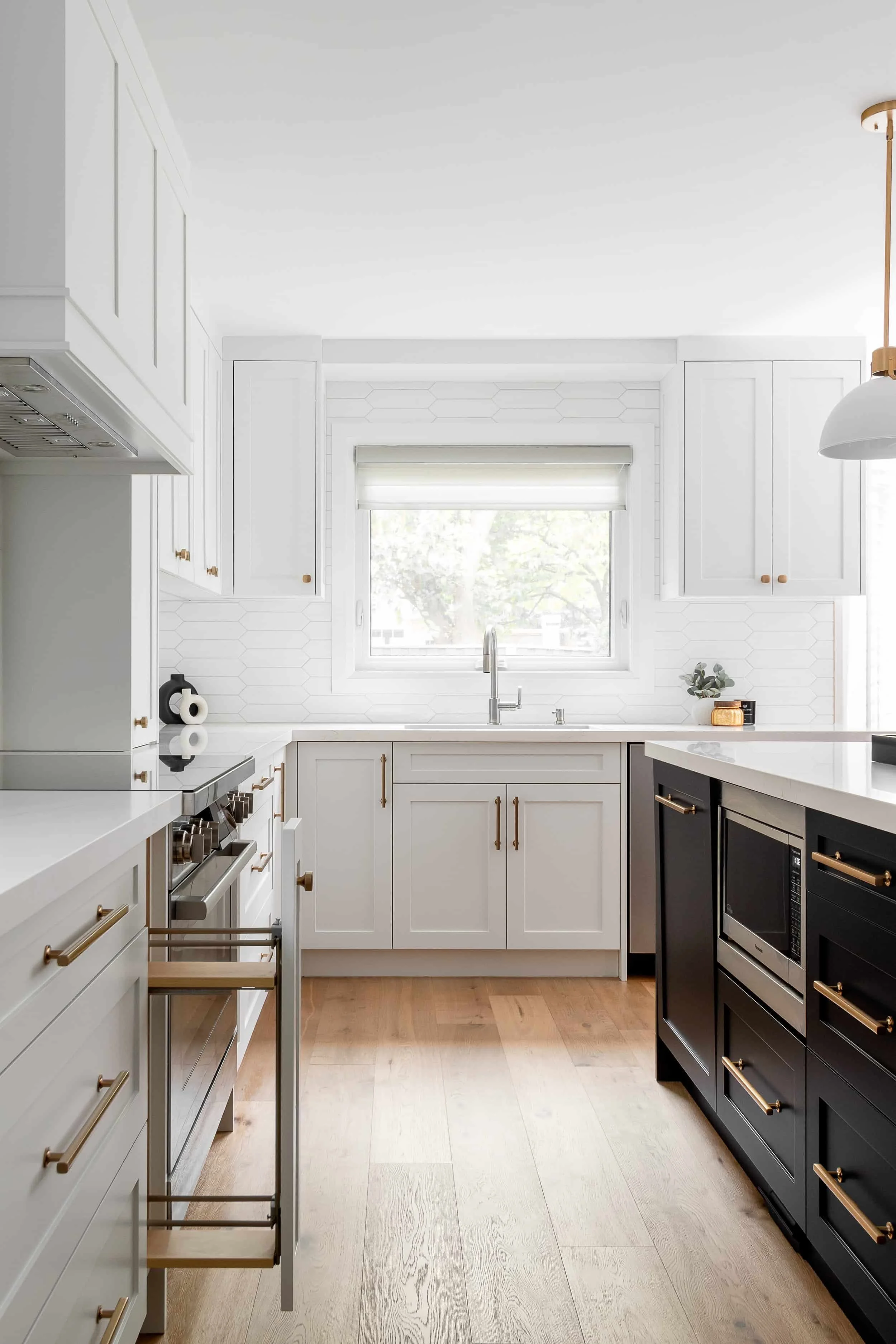 Modern kitchen with white and black cabinets, wooden flooring, and a window above the sink.