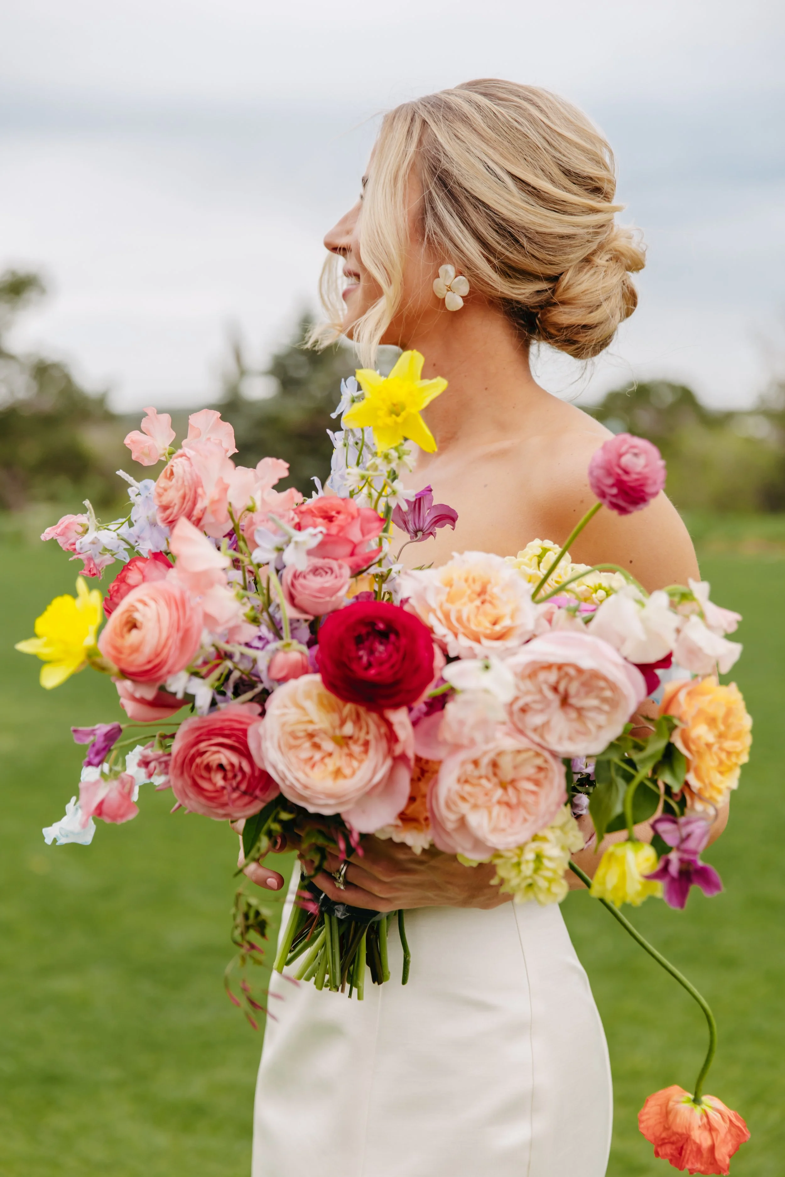 A woman in a white dress holding a large bouquet of colorful flowers with a blurred outdoor background.