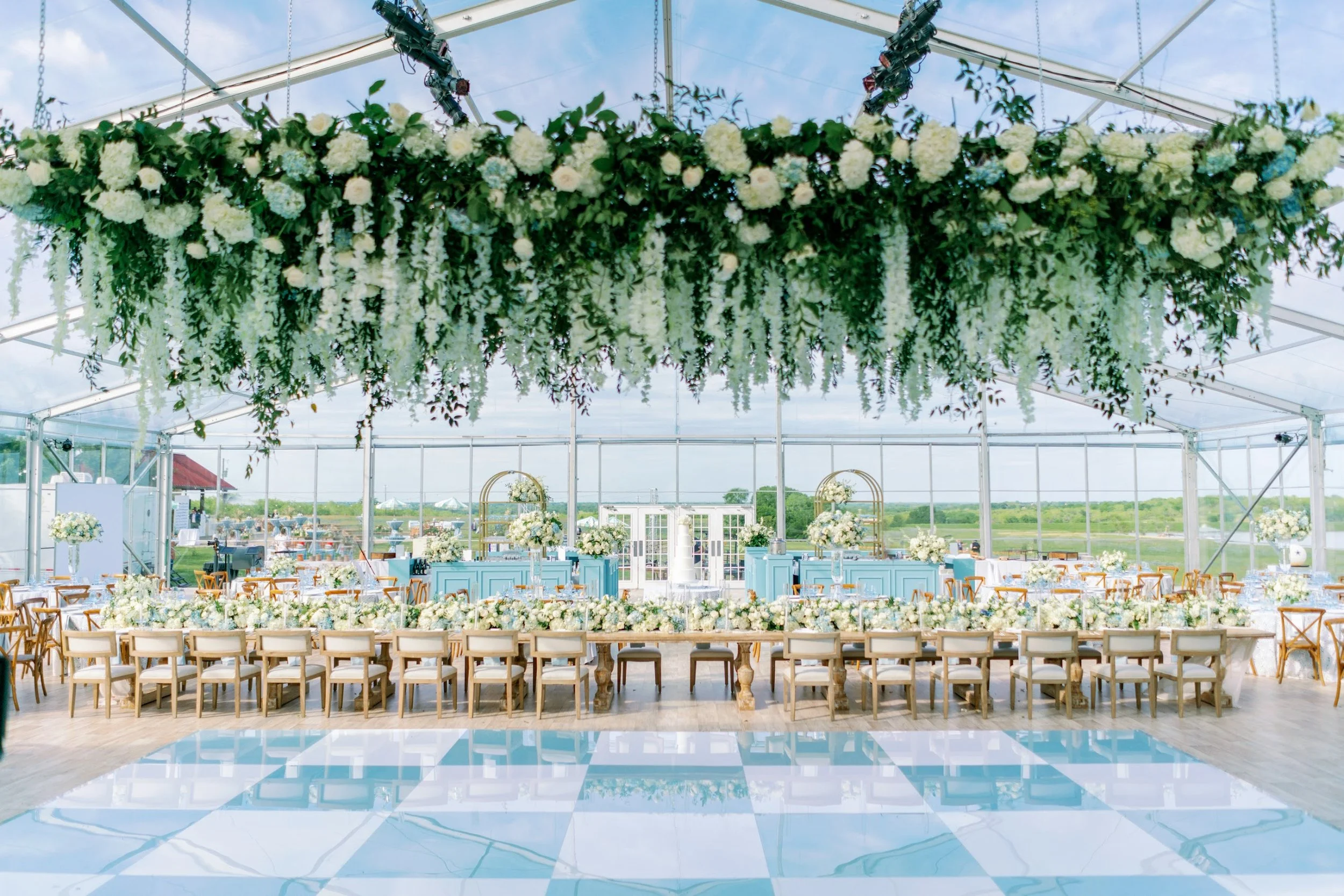 Tented wedding reception decorated with floral arrangements and canopy overhead, with a checkered dance floor in the foreground.