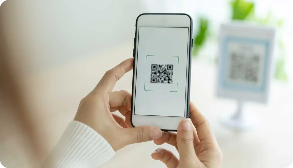 A guest scanning a QR code at a hotel front desk reception area, demonstrating how properties track campaign attribution and increase in-stay experience bookings.