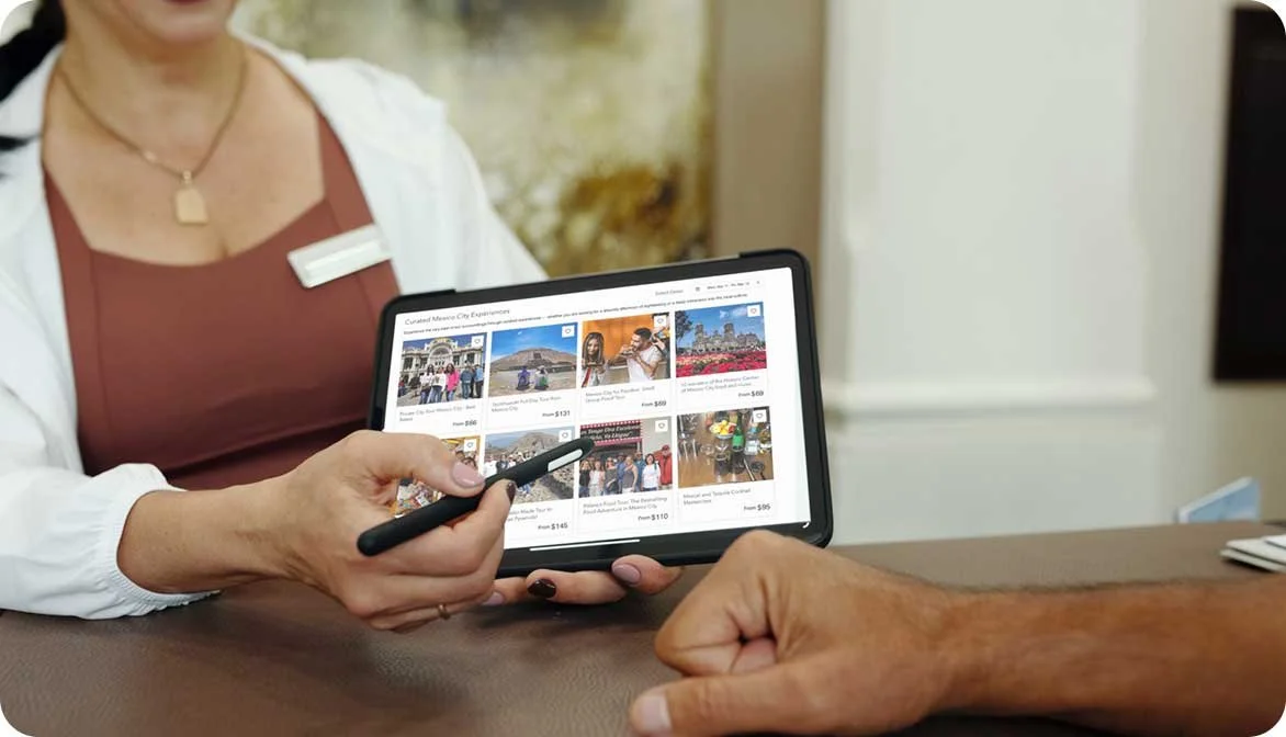 A hotel concierge using a tablet to show a guest bookable local tours and attractions, illustrating how hospitality properties generate incremental revenue through in-stay experiences.