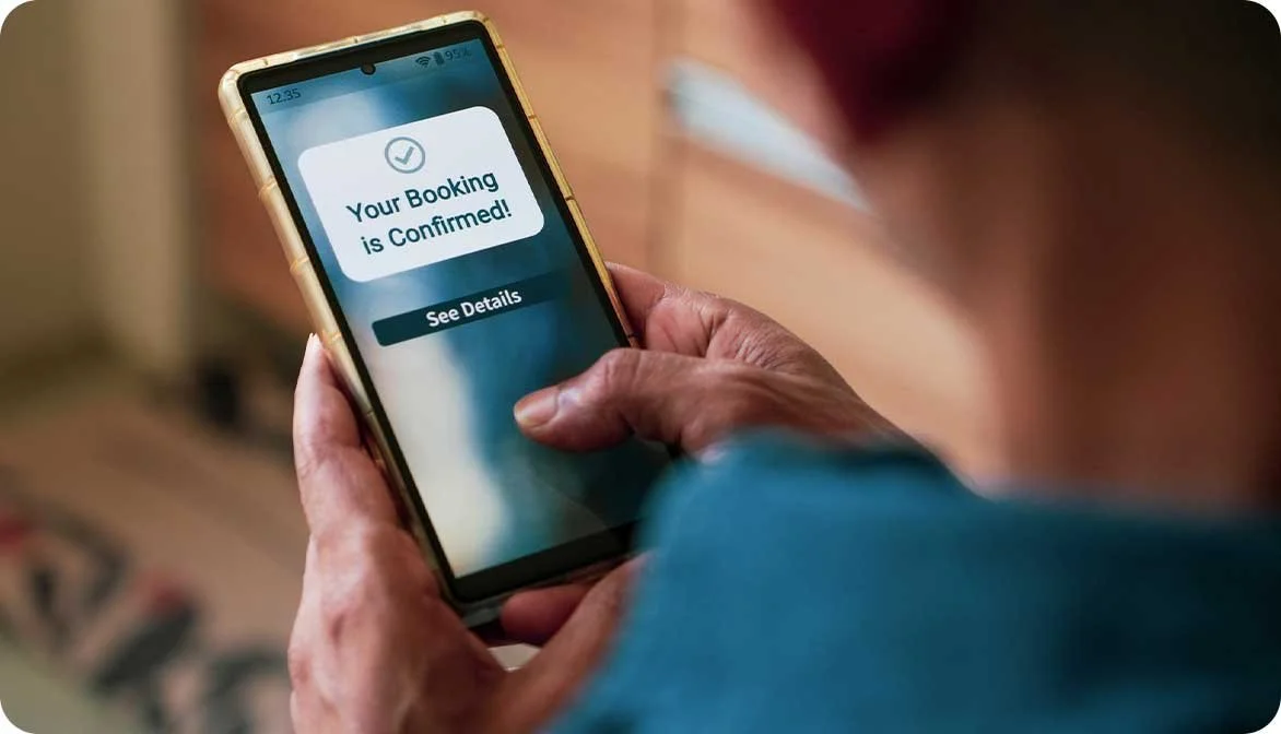 A close-up of a person holding a smartphone showing a booking confirmed notification, illustrating how transitioning from freesale to reserved inventory ensures real-time reliability.