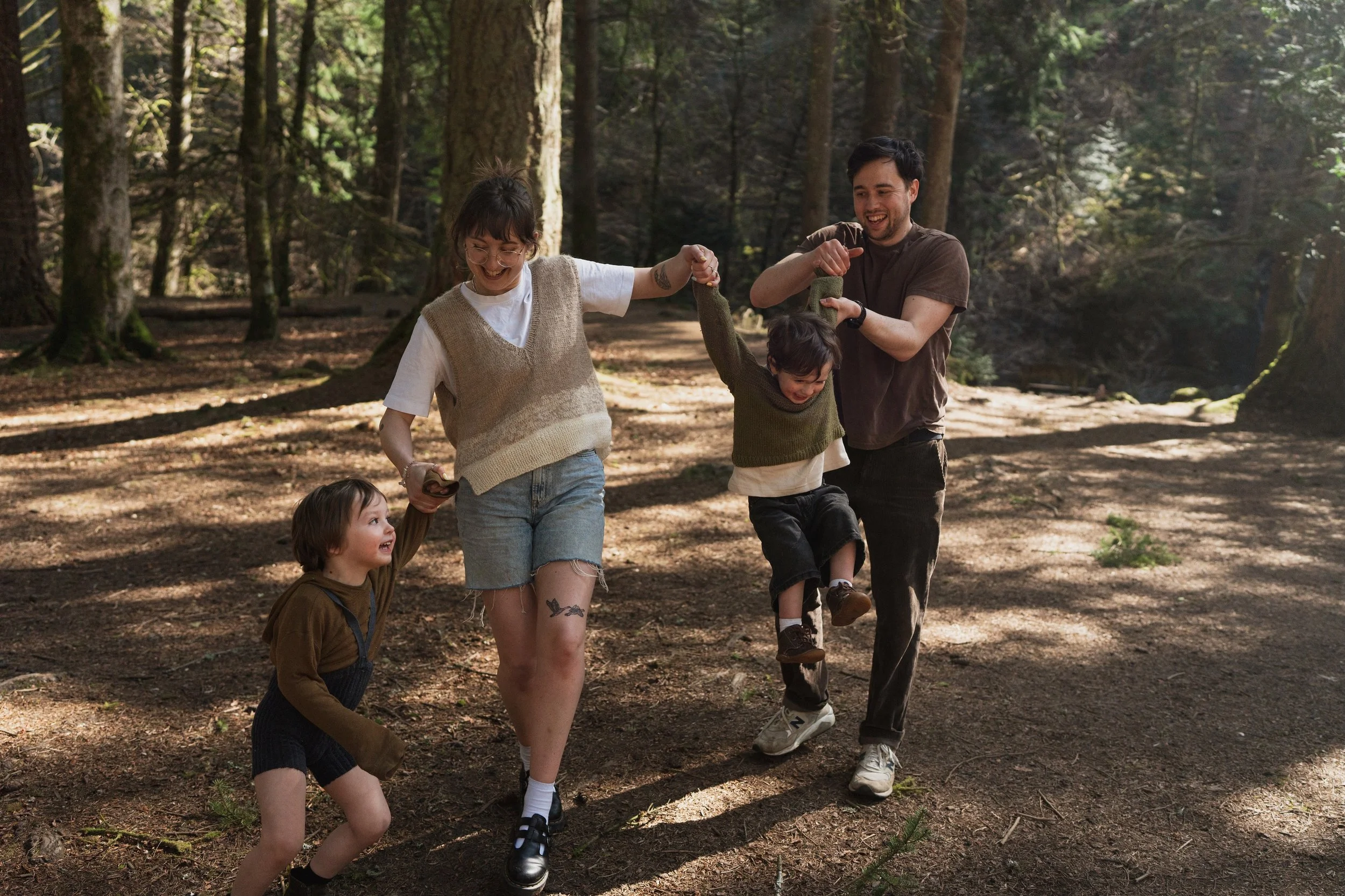A group of five people, including a child, walking in a forest with tall trees, holding hands and smiling, enjoying nature.
