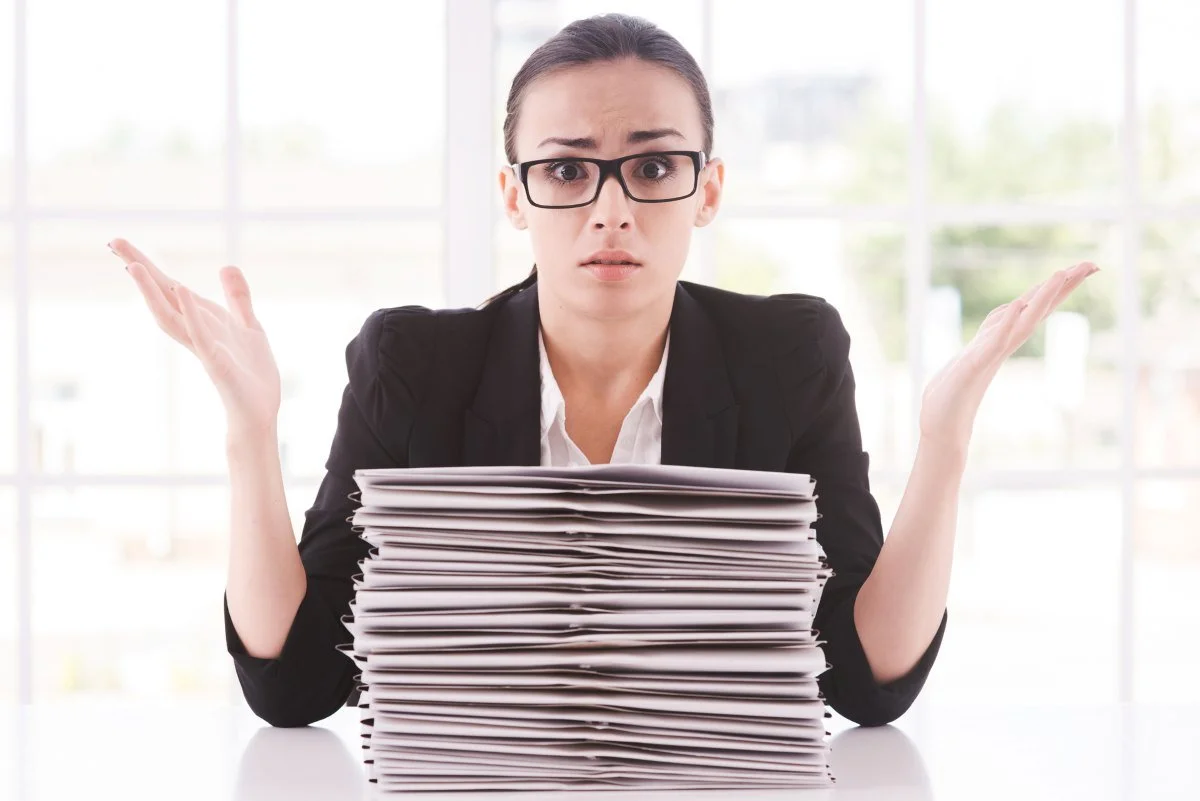 Hopeless businesswoman. Depressed young woman in suit tie looking at the stack of paperwork and gesturing while sitting at her working place