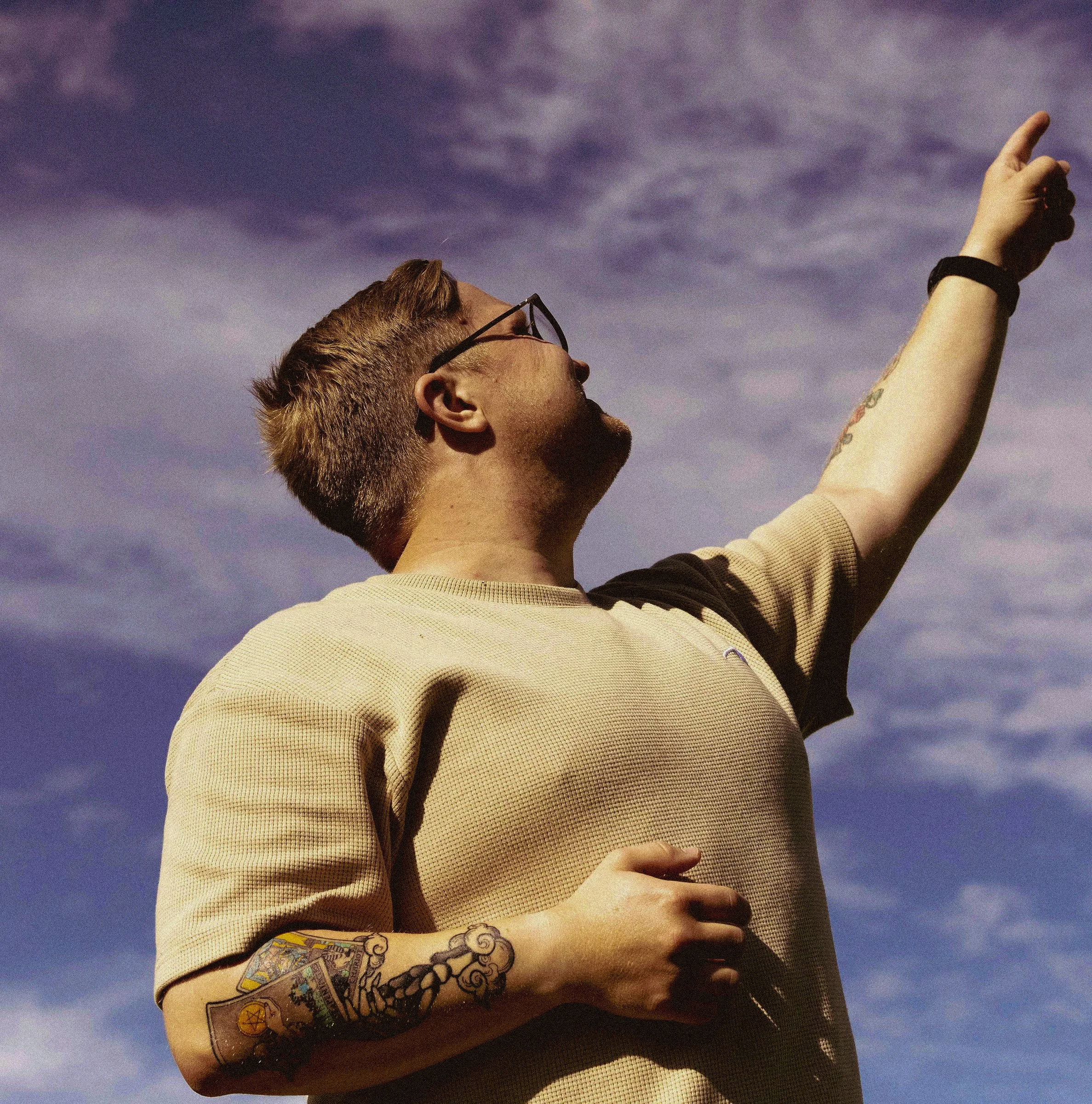 En man i solglasögon pekar mot himlen under en molnig dag.