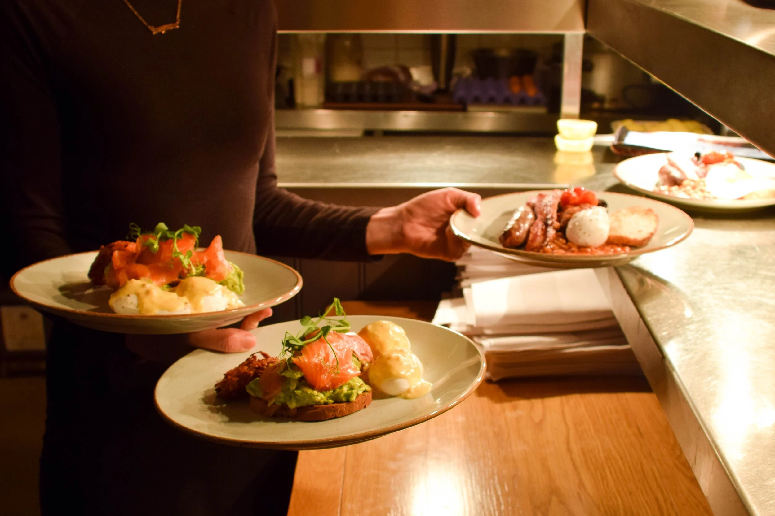 A person holding three plates with various brunch dishes in the restaurant, with a focus on the plates of food.