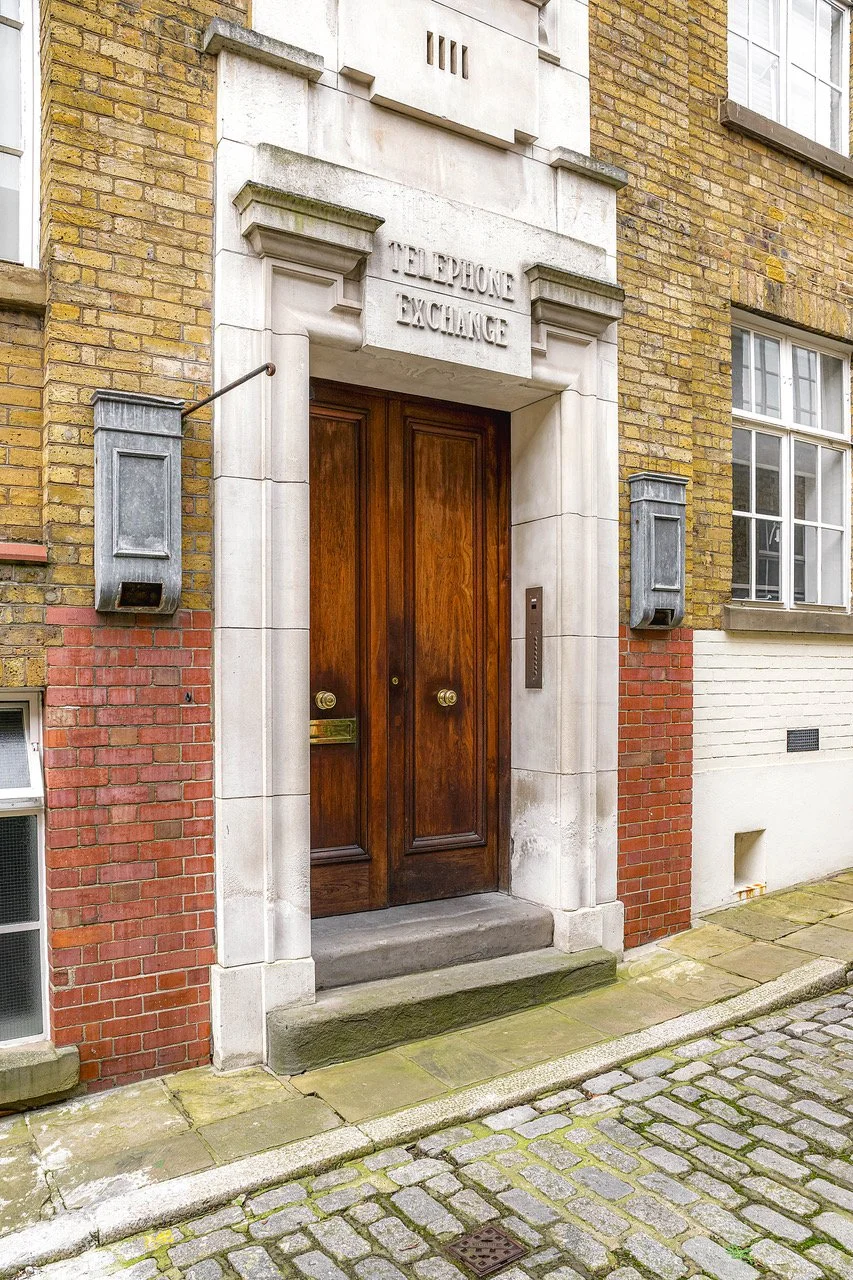 Wooden double door entrance to a building with stone and brick facade, labeled 'Telephone Exchange'.