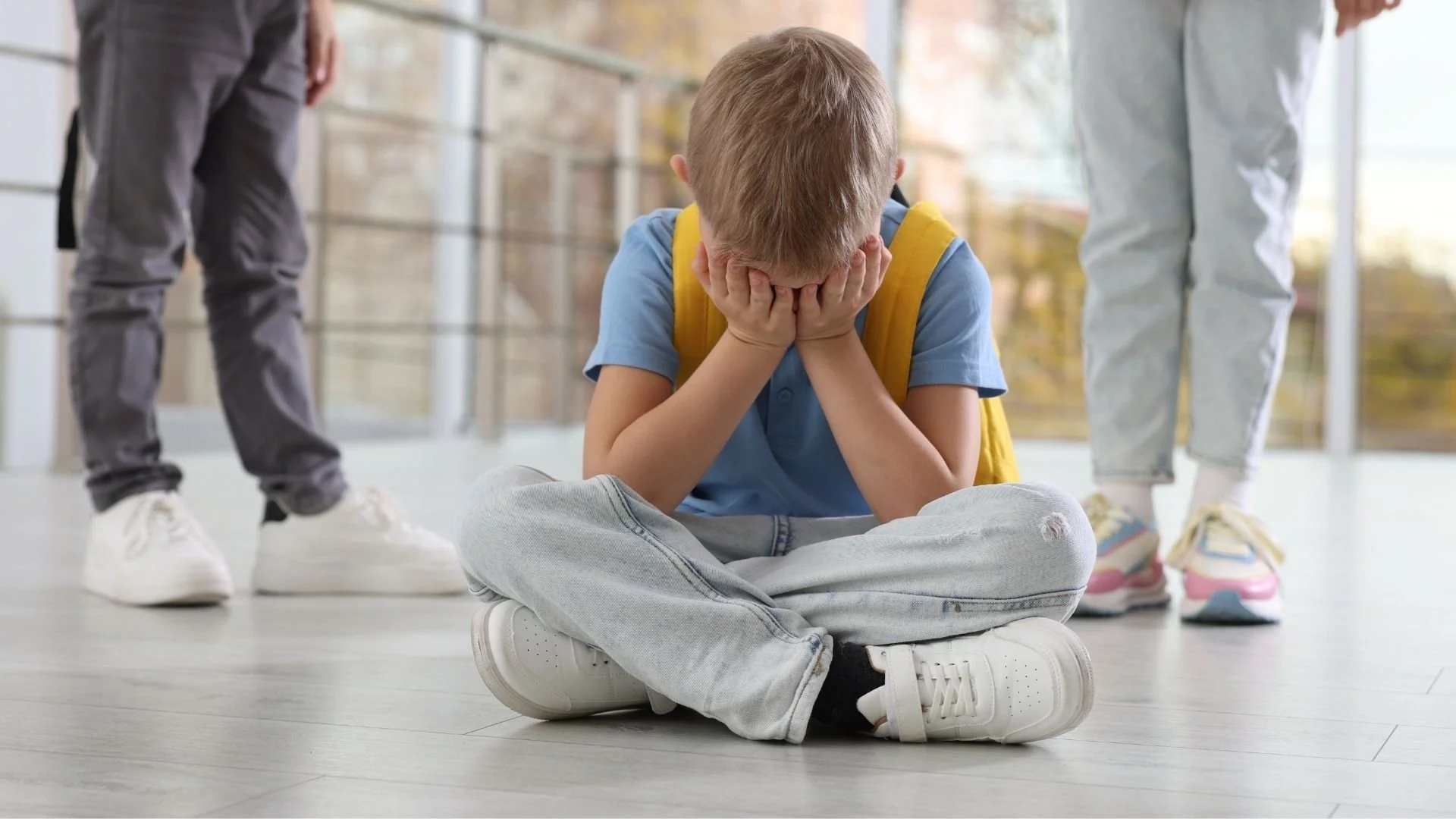 child with face in hands crying on the floor after being bullied in school
