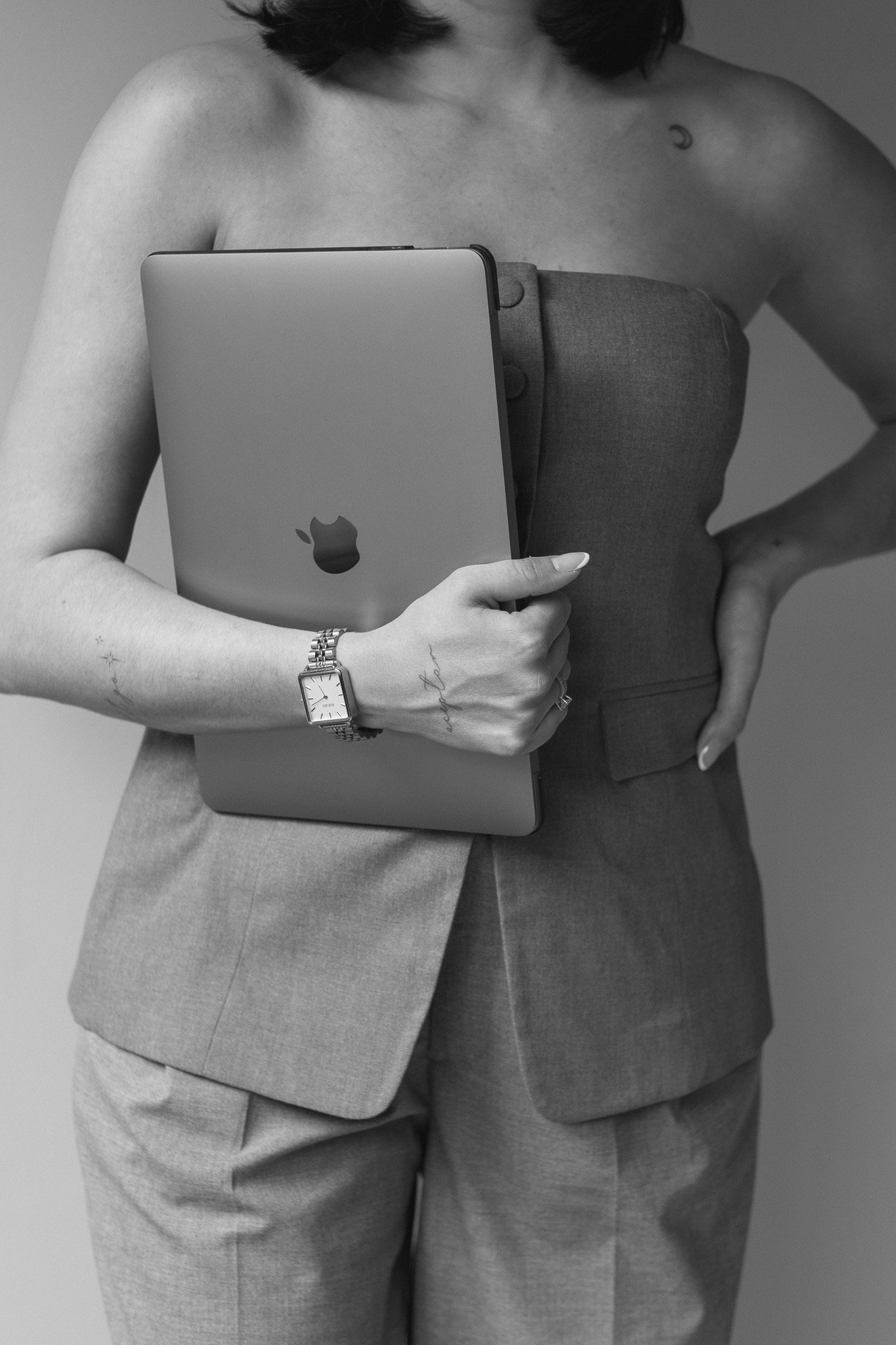 Personal Branding Foto, das eine starke, selbstbewusste Frau im Anzug zeigt, die einen Laptop unter dem Arm trägt