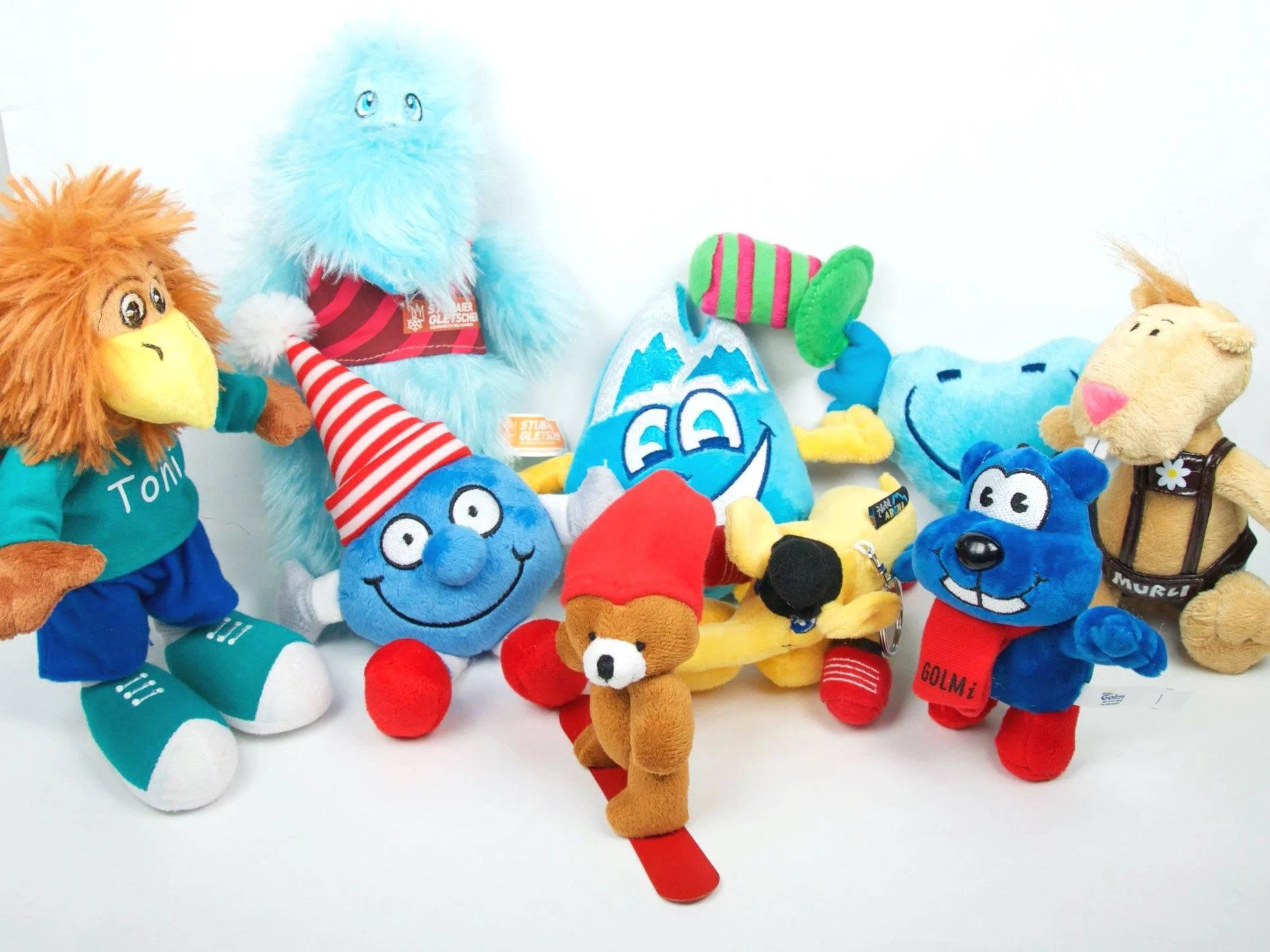 Verschiedene bunte Plüschtiere, darunter Affen, Gnome, Hund, Katze und andere, auf weißem Hintergrund.