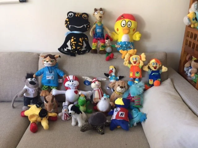 Verschiedene Plüschspielzeuge und Figuren, darunter bekannte Charaktere wie Doc McStuffins, Pinguin, Hund, Katze, und andere Tiere und Figuren auf einer Couch.