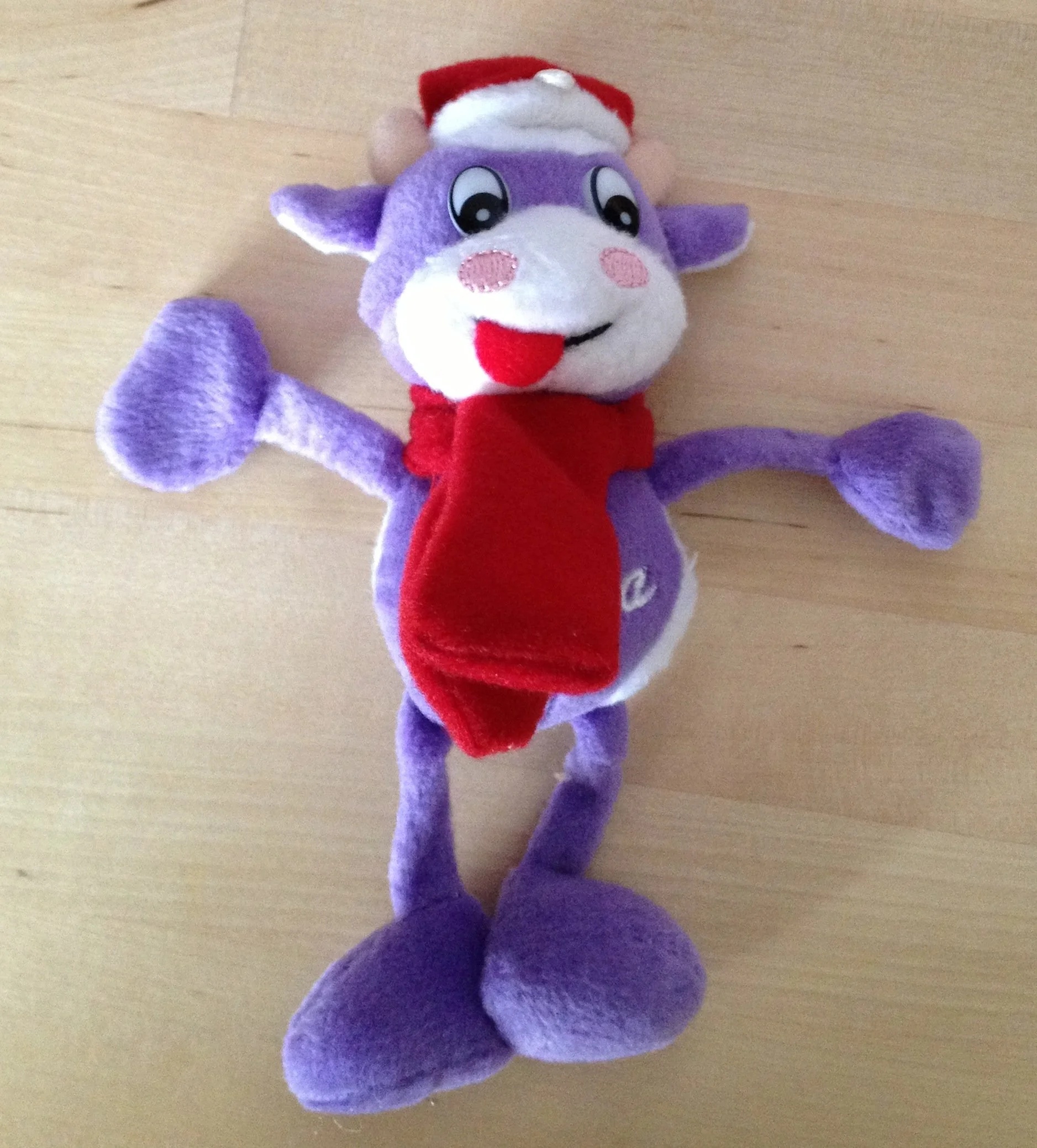 Lustiges Plüschspielzeug eines lila Hasen mit Weihnachtsmannmütze, roter Weste, großen Füßen mit langen Ohren und einem fröhlichen Gesicht, das auf einem Holztisch liegt.