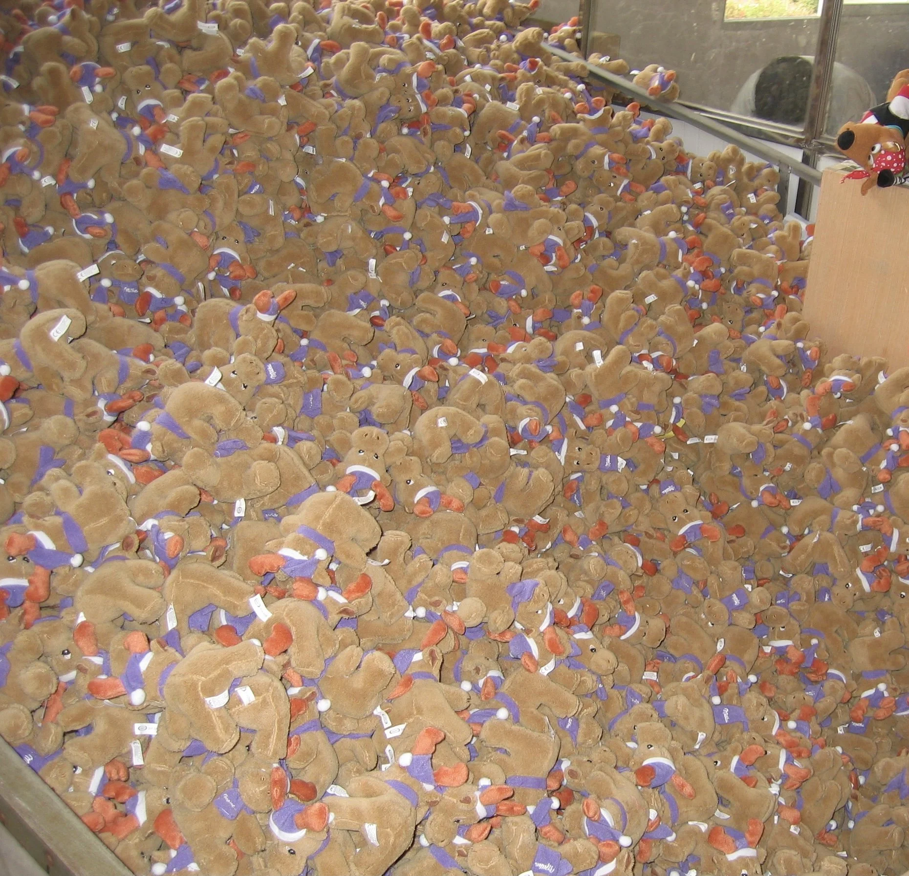 Viele Teddyfiguren mit blauen Westen, roten Mützen und weißen Schals in einer Klammermaschine