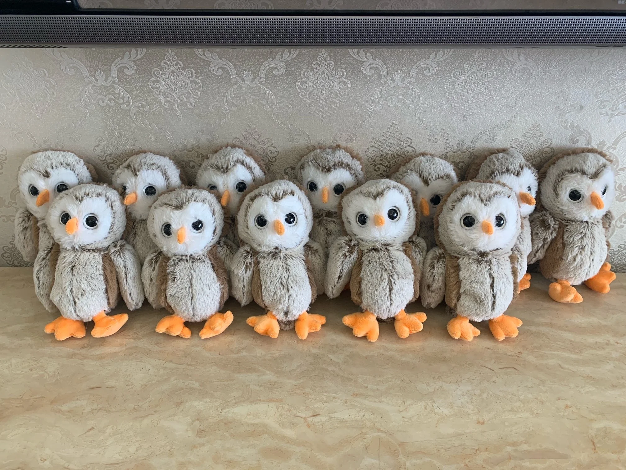 Mehrere kuschelige Stofftiere, die Eulen darstellen, stehen auf einer Holzfläche vor einer gemusterten Wand.