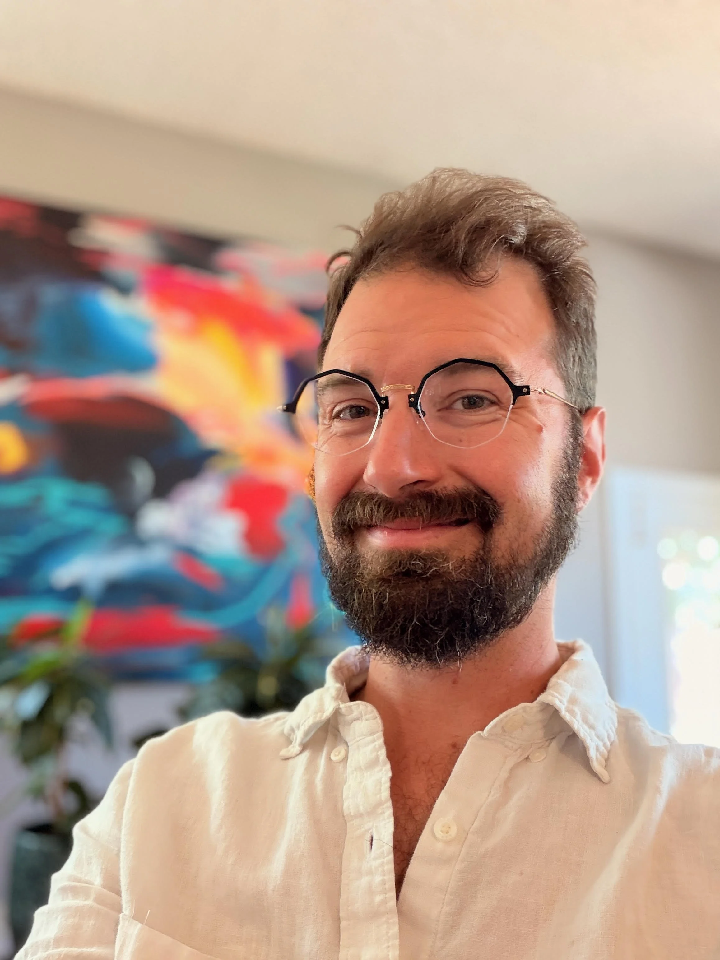 a therapist with short brown hair, glasses, and a brown beard smiling at the camera