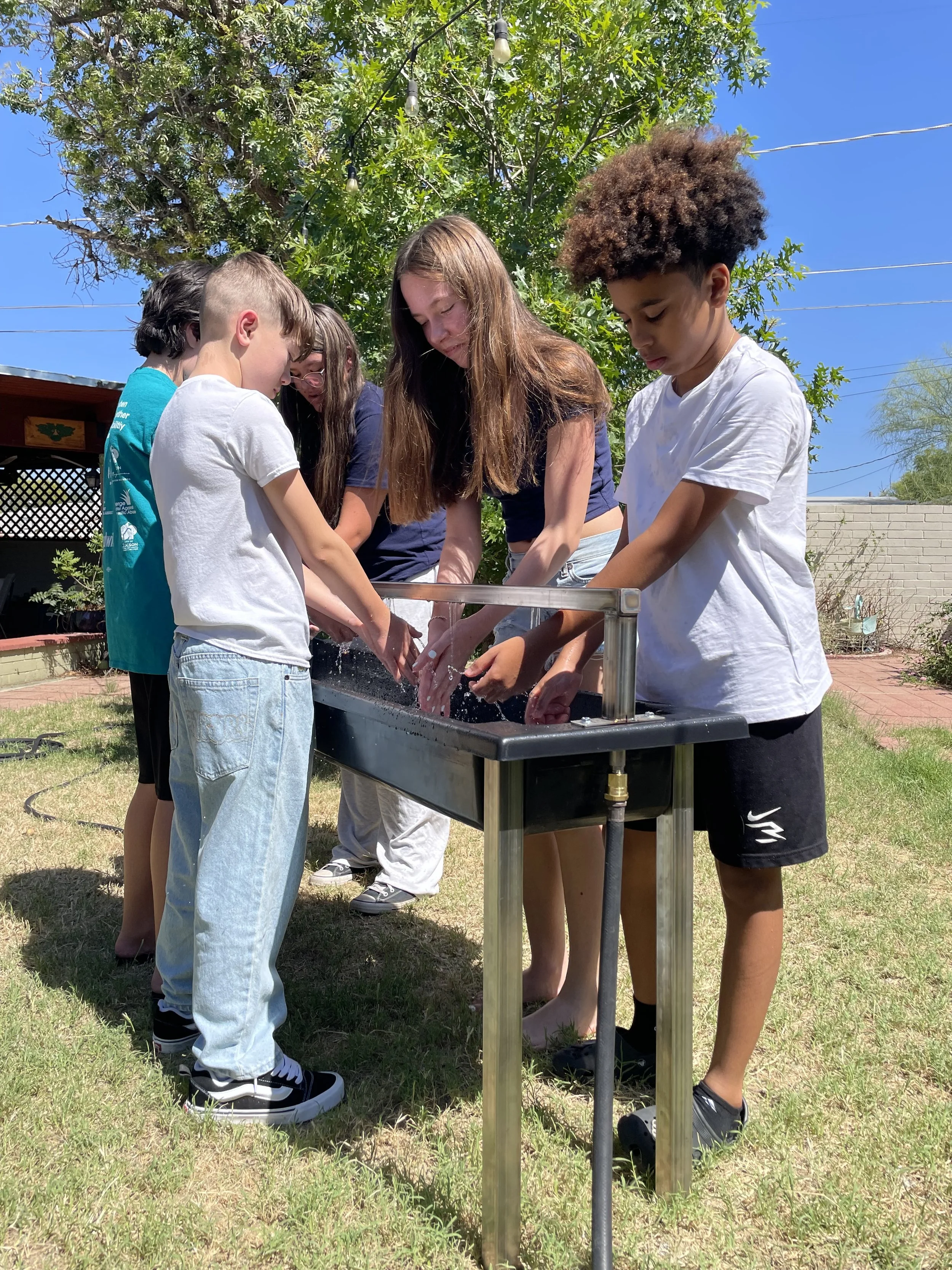 Students washing hands at an outdoor handwashing station in the sunshine