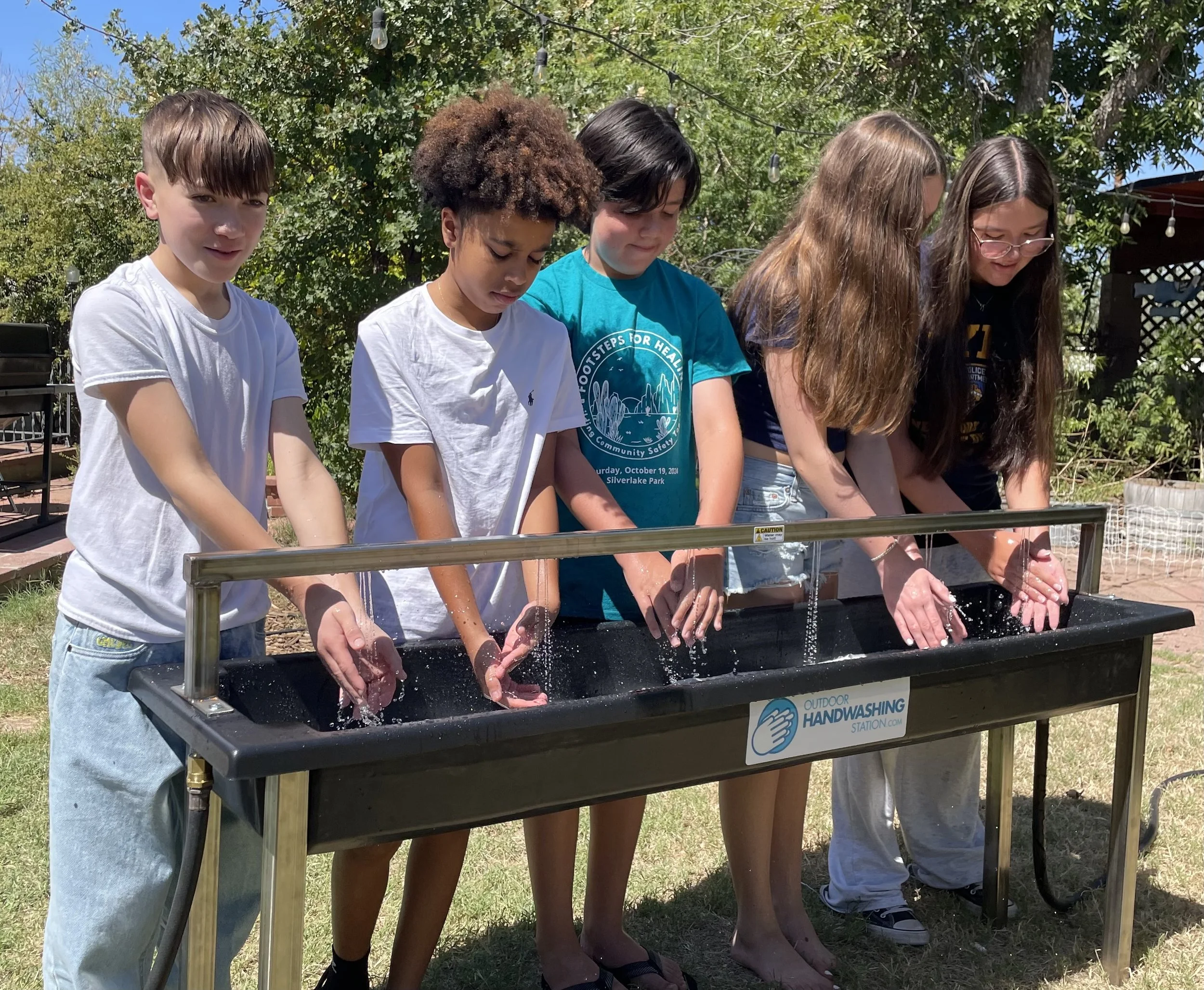 Students washing hands at an outdoor handwashing station in the sunshine