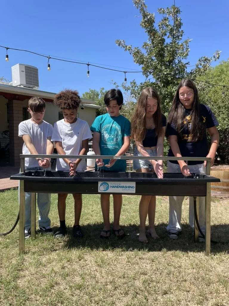 Students using a multi-person outdoor handwashing station, accessible for all ages including wheelchair users