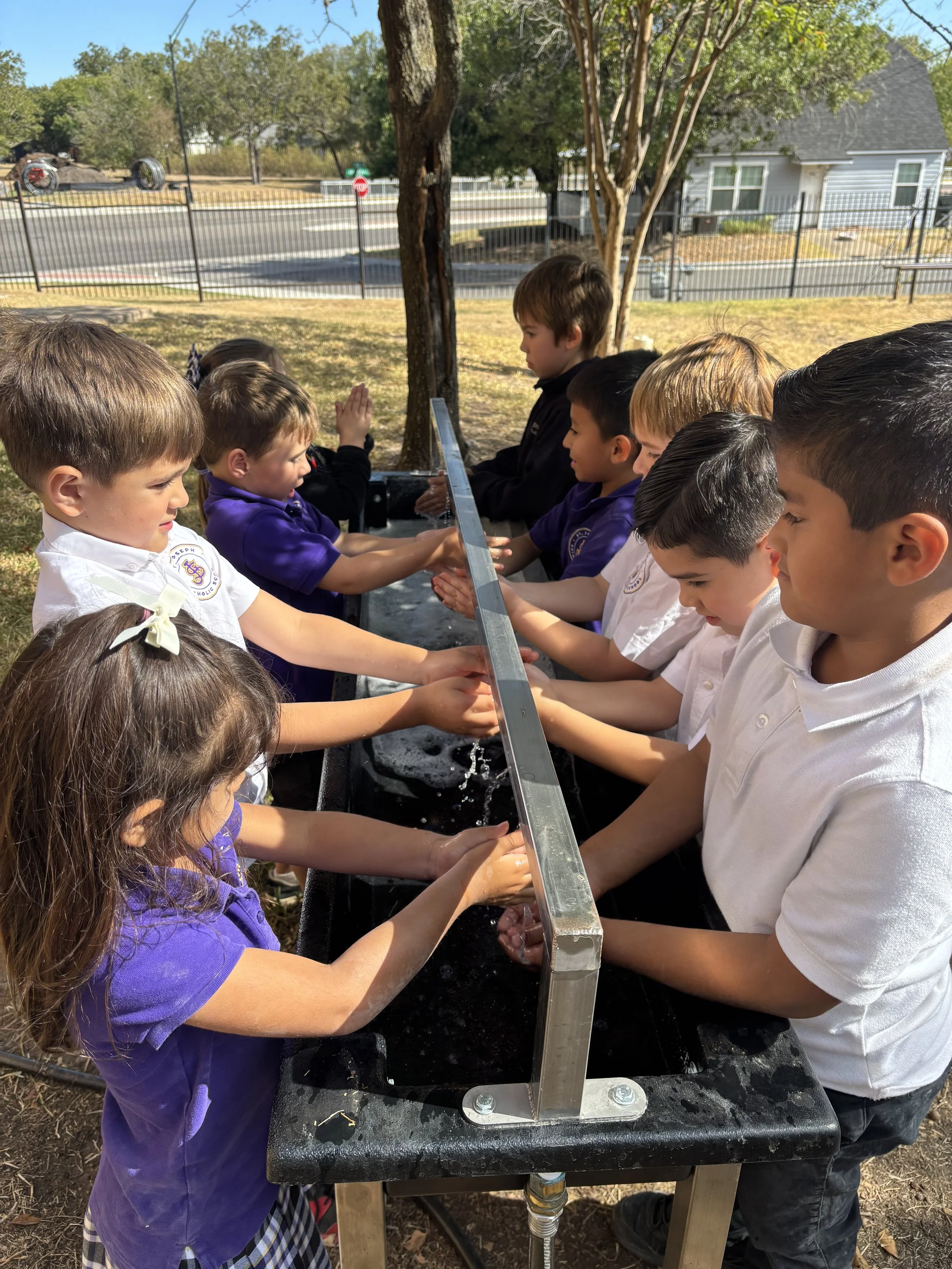School children washing hands at a 6 person outdoor handwashing station.