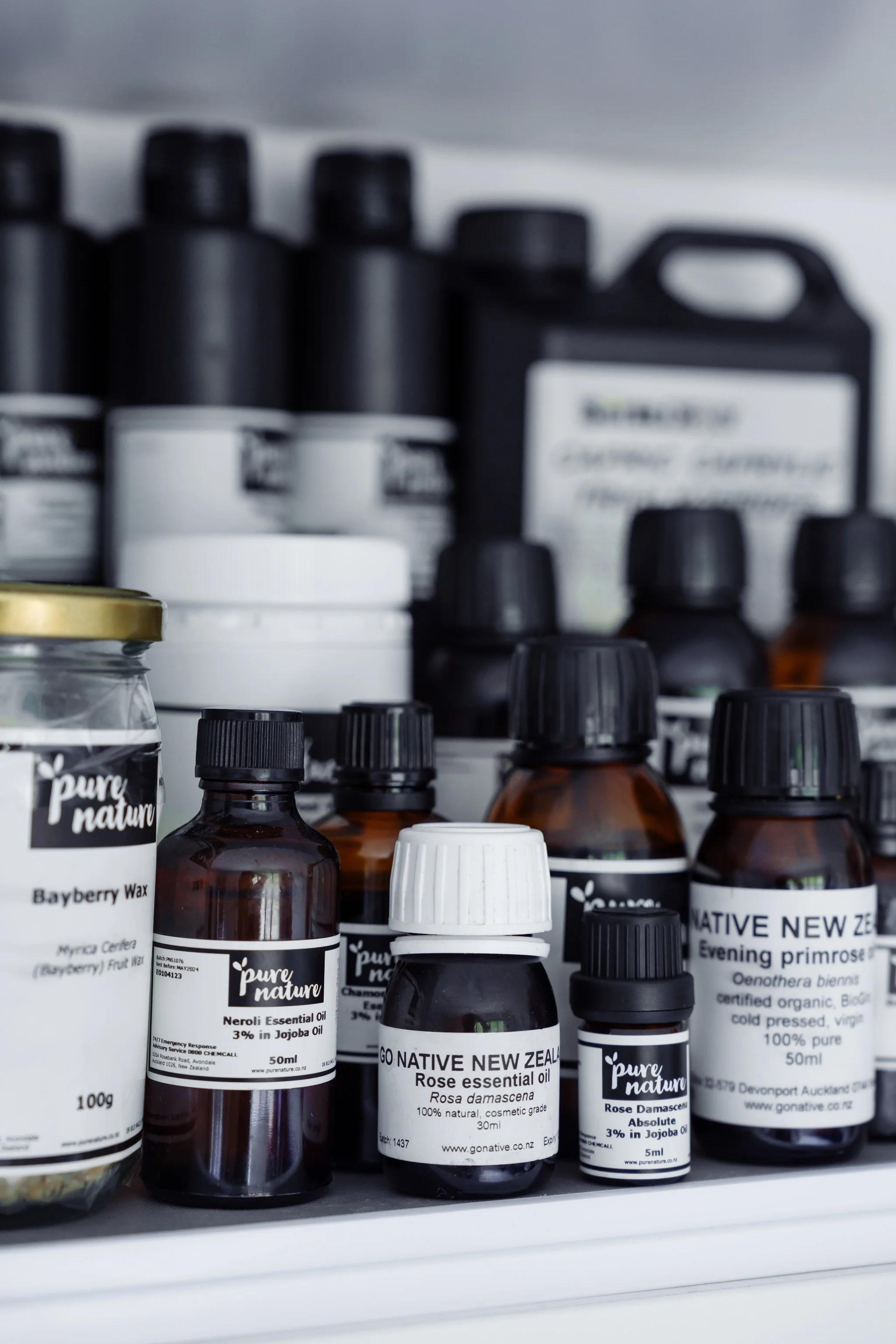 Various bottles and containers of essential oils and natural products from brands like "Pure Nature" and "Go Native New Zealand," including items like Bayberry Wax and Rose Essential Oil, arranged on a shelf.