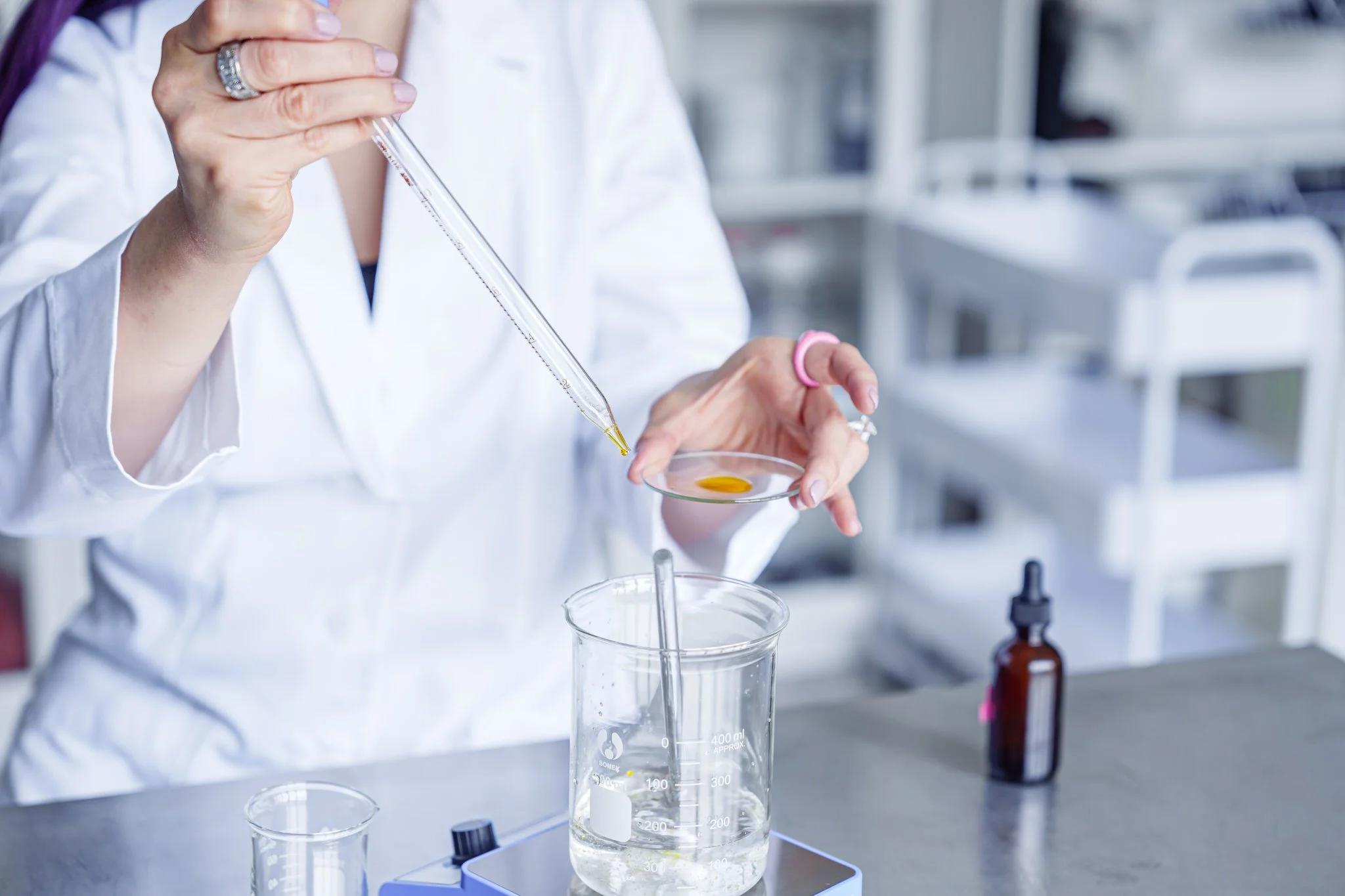 Scientist in lab using pipette to add liquid to glass slide over beaker with solution.
