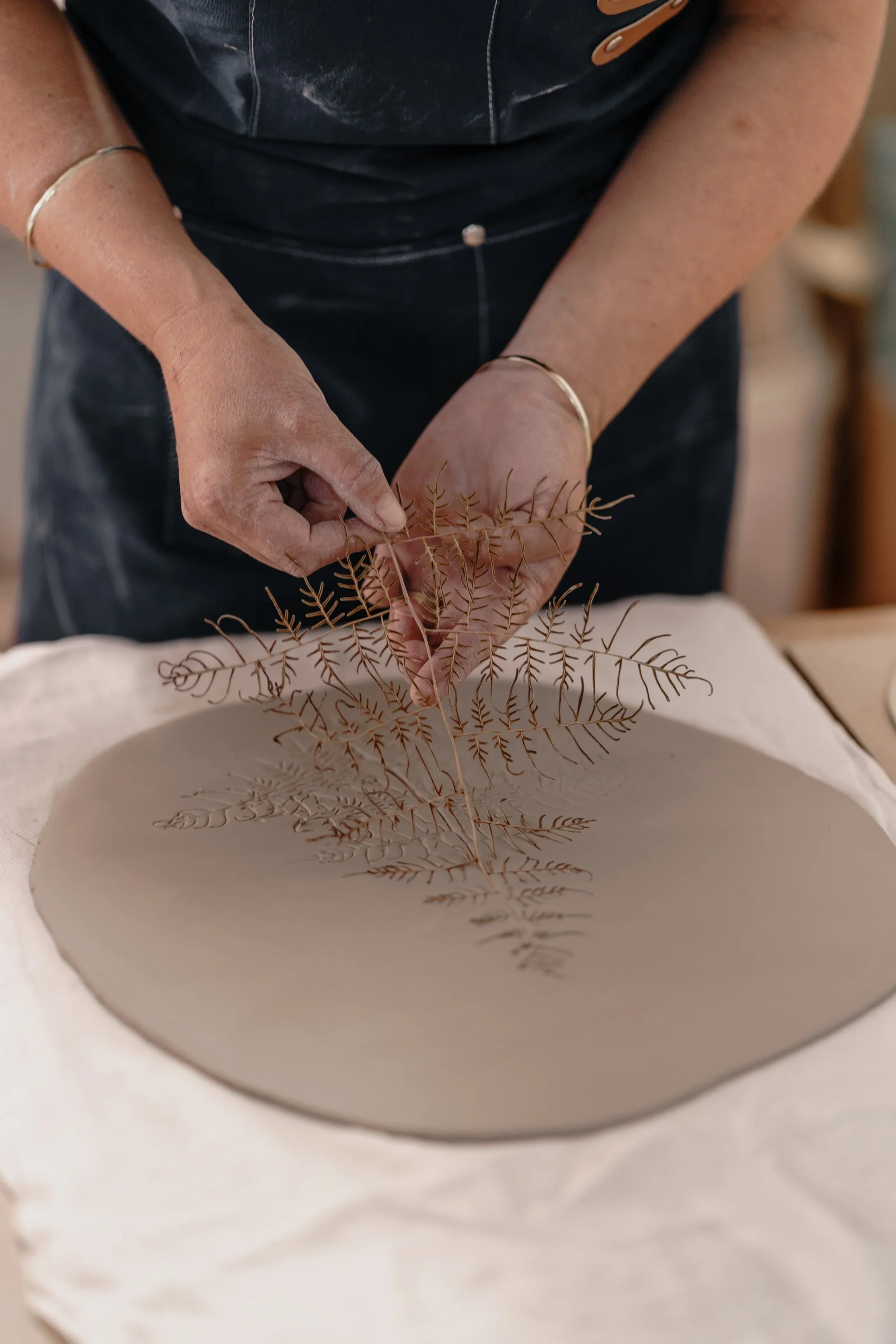 Person imprinting a fern leaf onto clay slab
