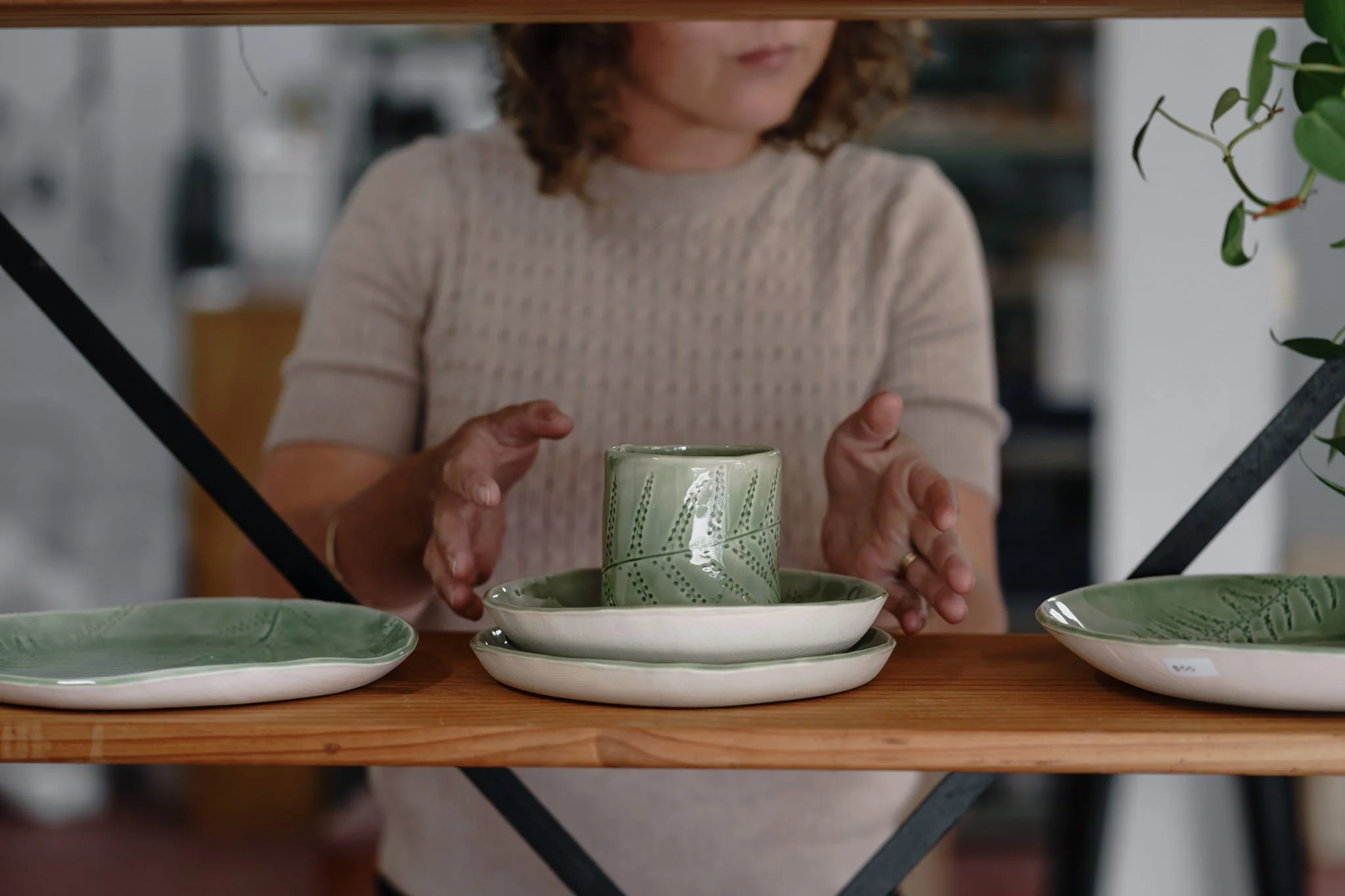 Person arranging green ceramic dishes on a wooden shelf.