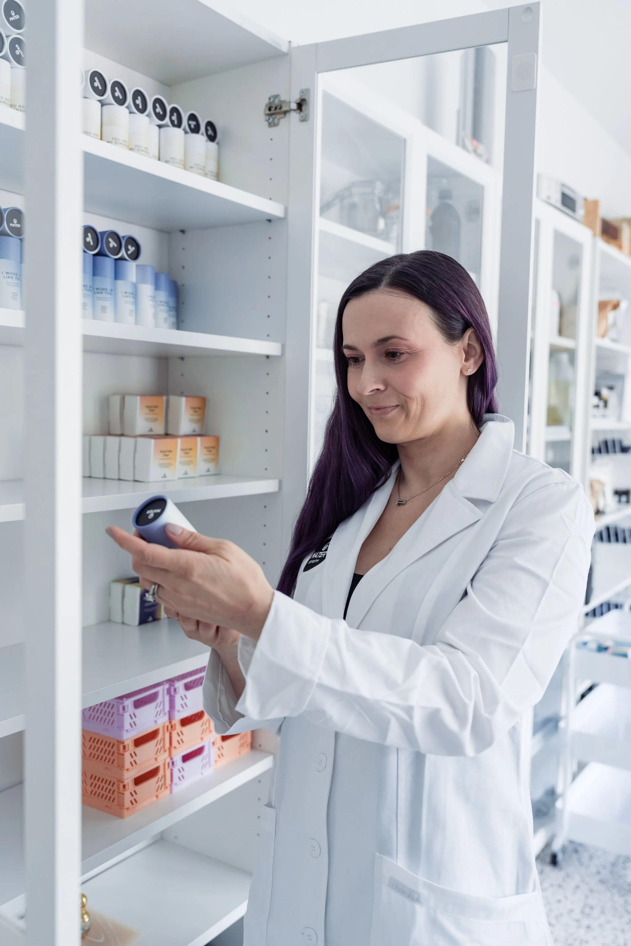 Woman in lab coat examining product bottle in cosmetic store with shelves of skincare products.