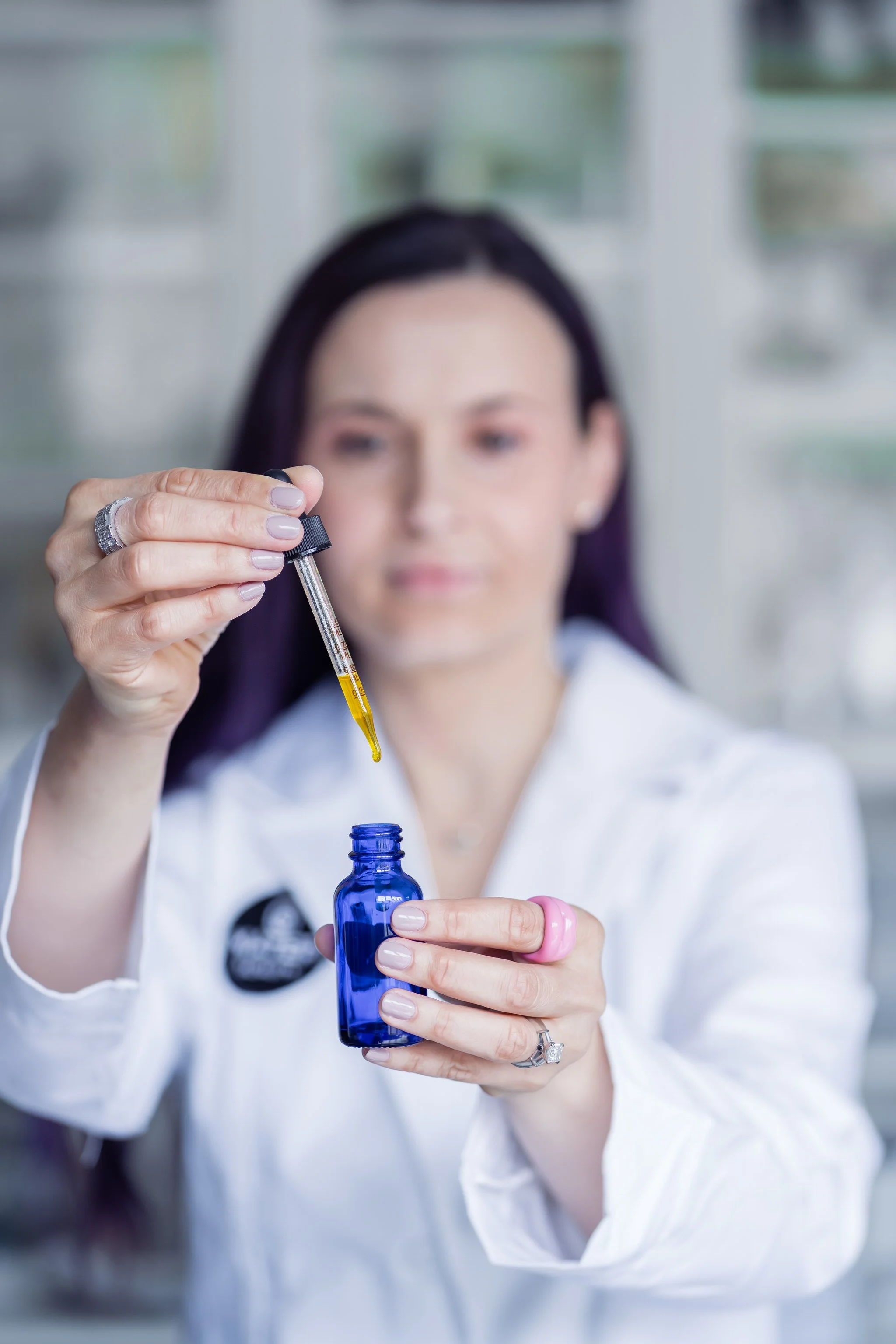 Person in lab coat using dropper with blue bottle
