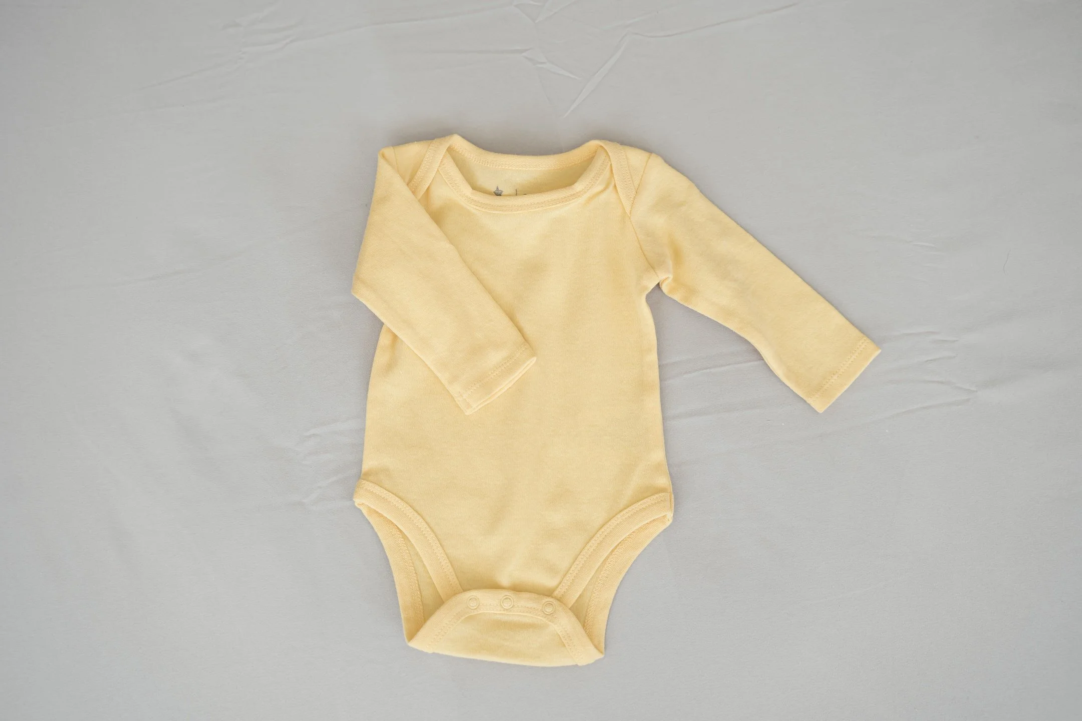 Yellow baby onesie with long sleeves on a gray background.