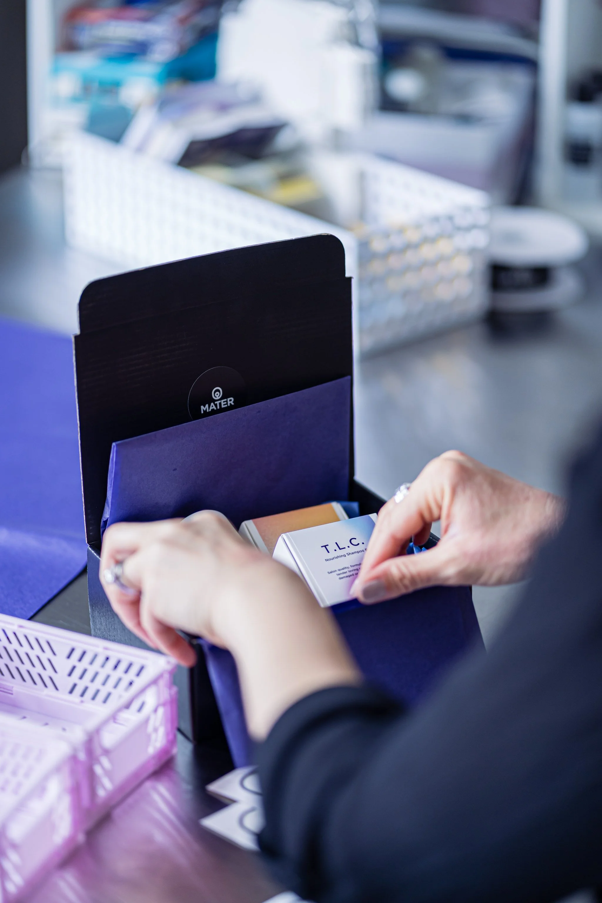 Person packaging a product labeled "T.L.C." into a black and blue box on a counter.