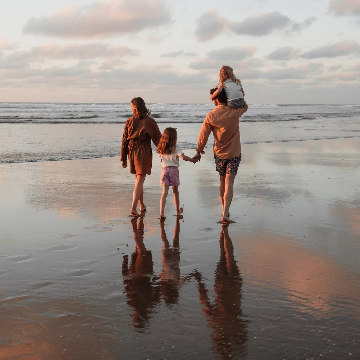 Family walking on a beach at sunset, with reflections on wet sand.